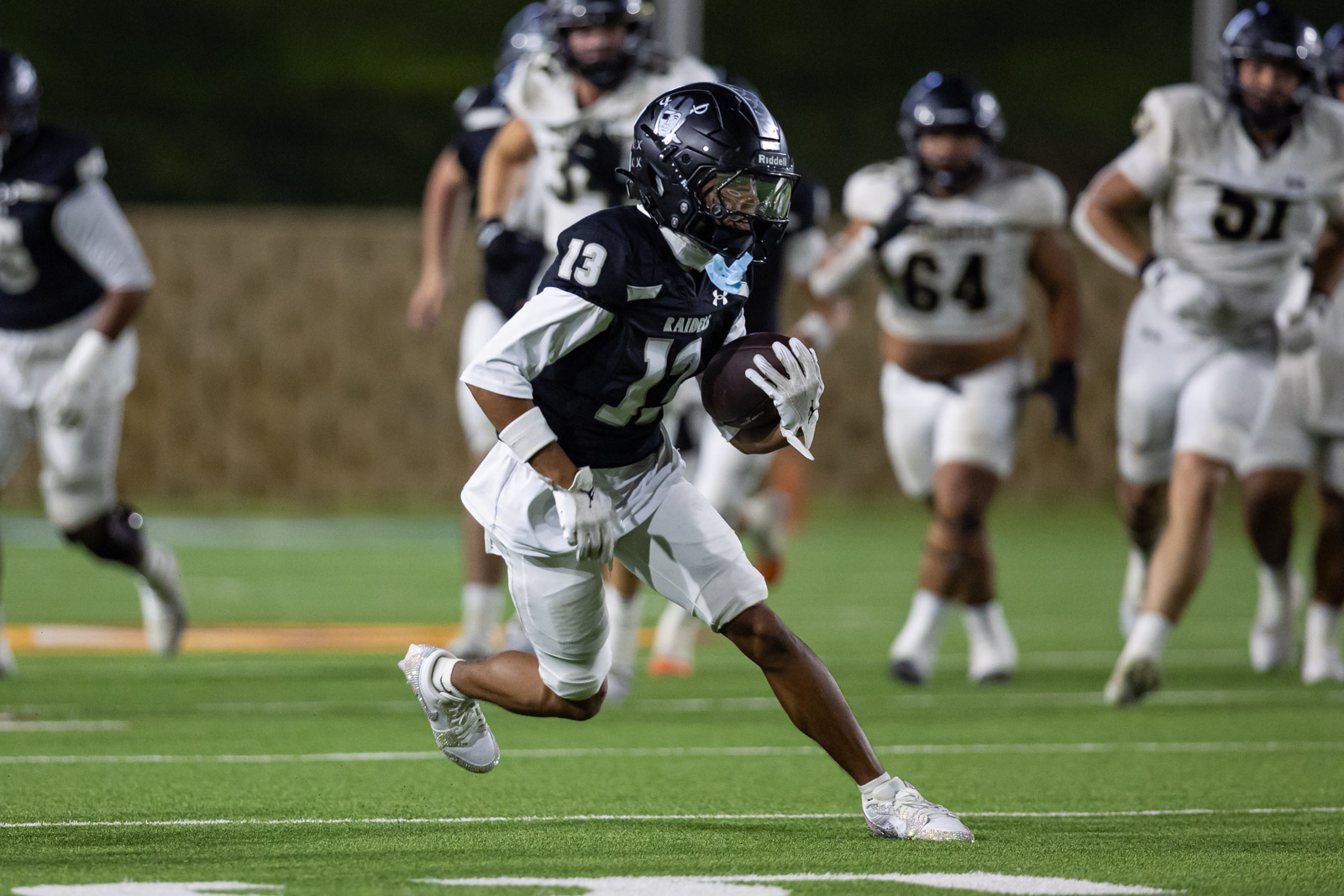 CHS-RHS-FB-43 | Press Pass Sports Football player #13 in black jersey runs with the ball on a nighttime field, chased by white-jersey defenders.