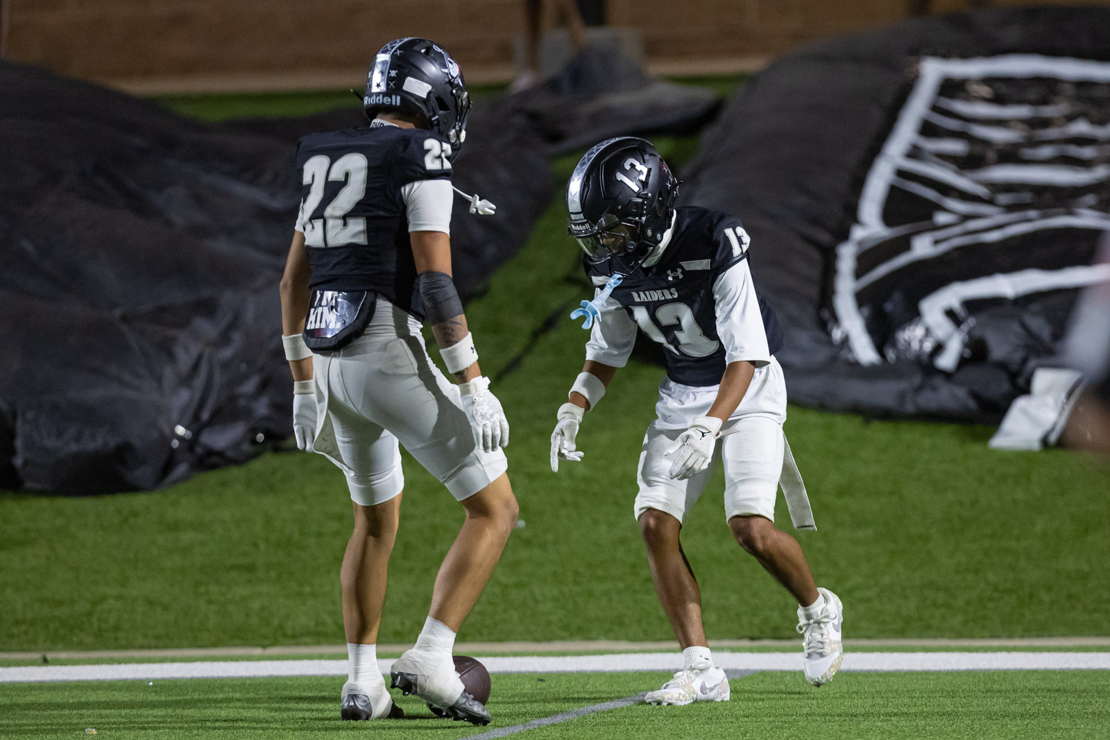 CHS-RHS-FB-45 | Press Pass Sports Two football players in navy jerseys and white pants stand near a loose football on a turf field during practice.