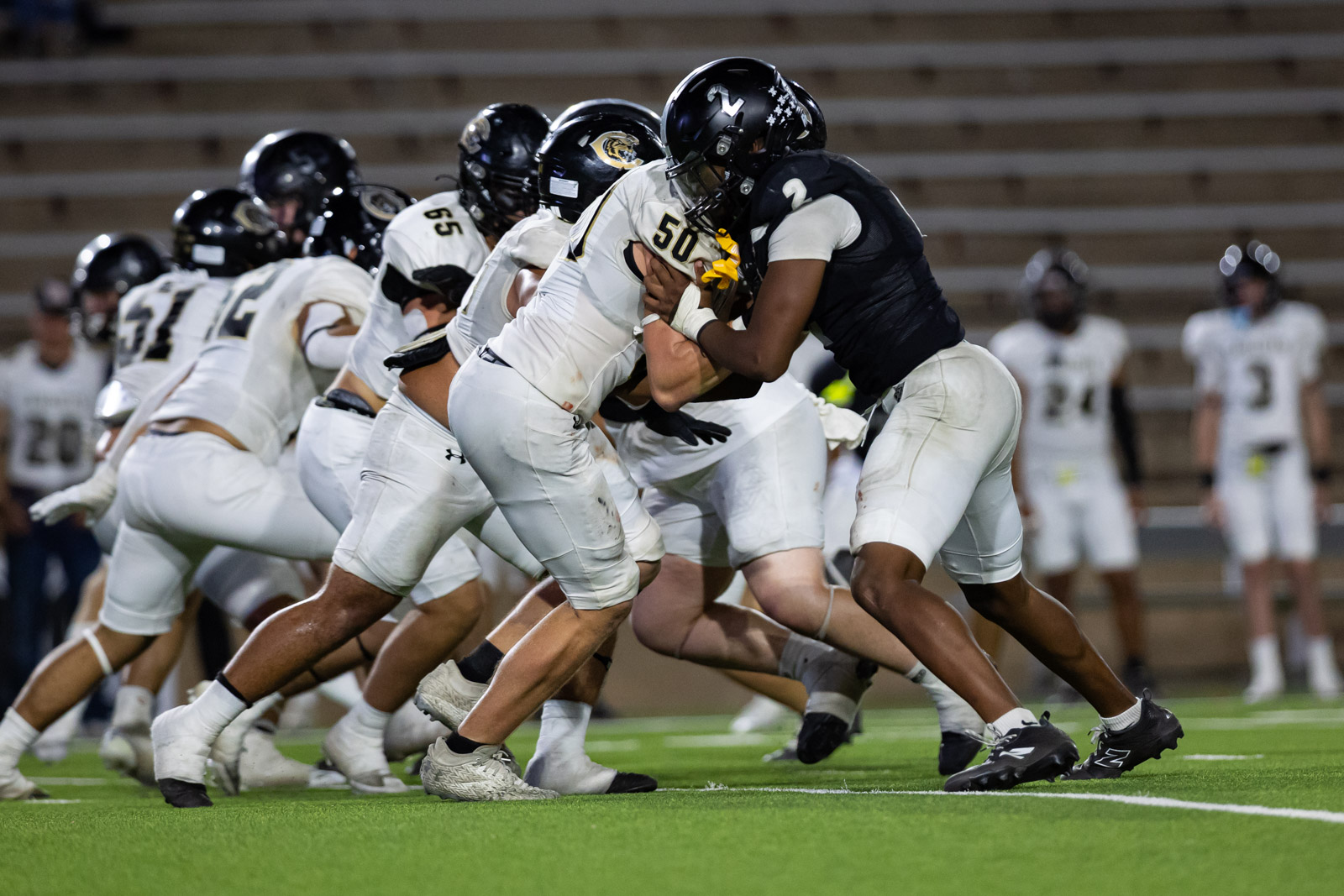 CHS-RHS-FB-52 | Press Pass Sports Football players in white and black uniforms collide at the line of scrimmage during a game on a green field.