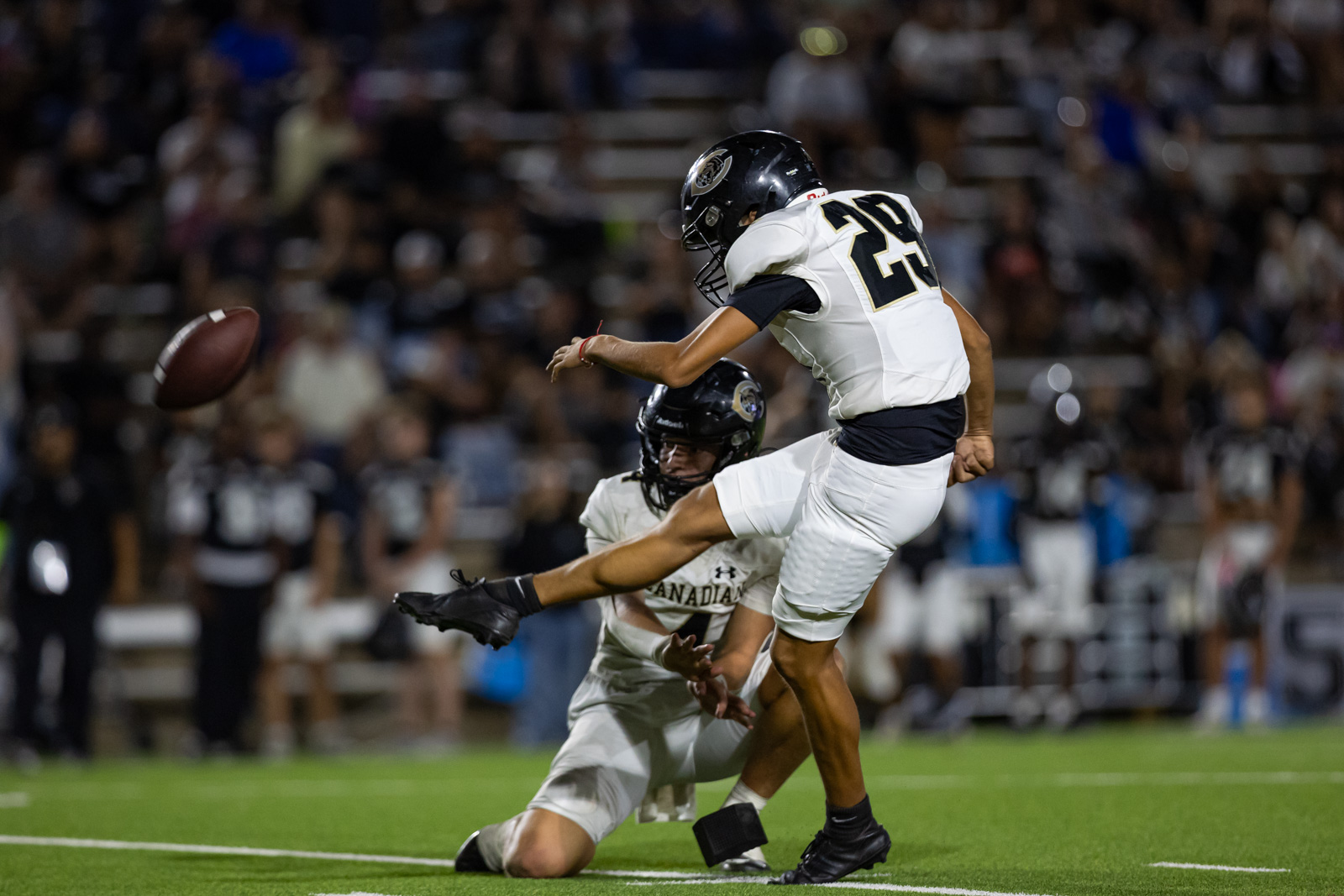 CHS-RHS-FB-55 | Press Pass Sports Football players in white uniforms contest a loose ball during a night game; one player leaps while another reaches for the ball with a stadium crowd in the background