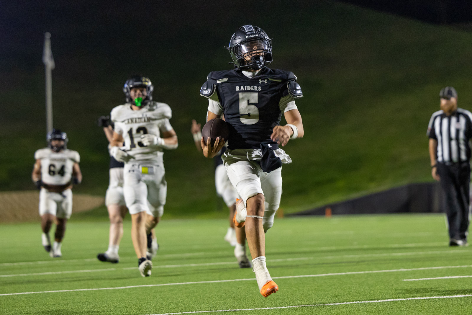 CHS-RHS-FB-56 | Press Pass Sports Football player wearing number 5 Raider uniform runs with ball on a night game, while defenders in white chase behind him.