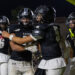 CHS-RHS-FB-58 | Press Pass Sports Football players in black Raiders uniforms celebrate on a night field, embracing each other after a play.