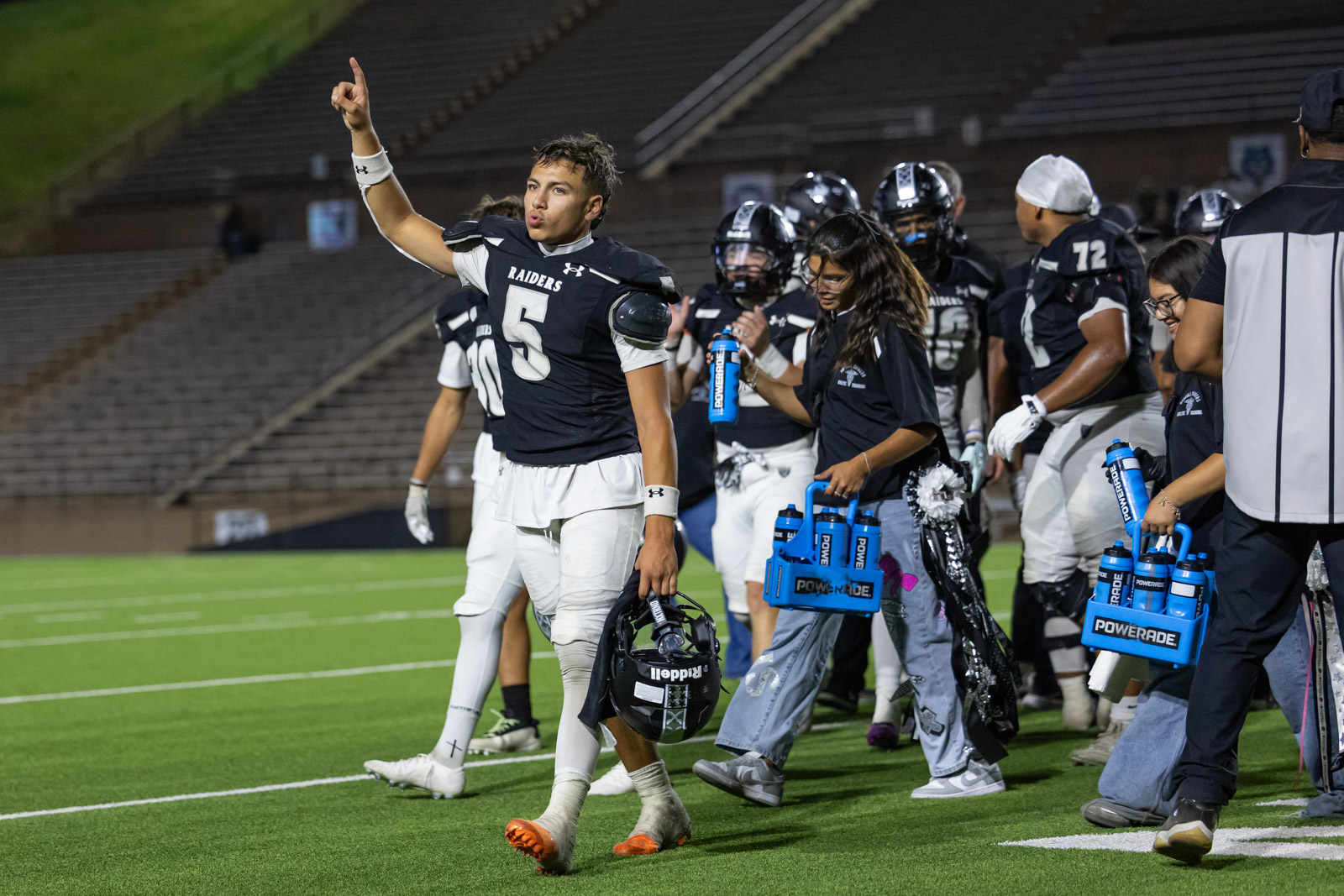 CHS-RHS-FB-60 | Press Pass Sports Football player in a black Raiders jersey #5 raises his index finger as he walks off the field, helmet in hand.