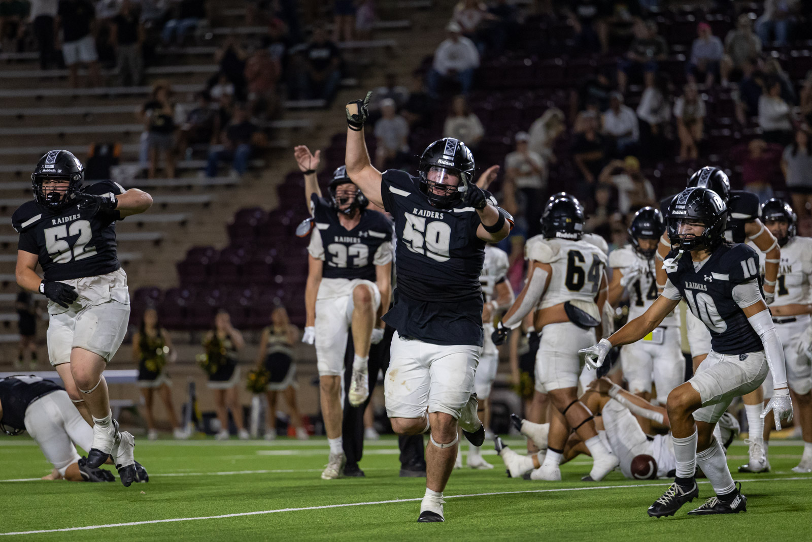 CHS-RHS-FB-61 | Press Pass Sports Raiders football players celebrate a touchdown on the field as teammates run and fans watch from the stands in a night game.