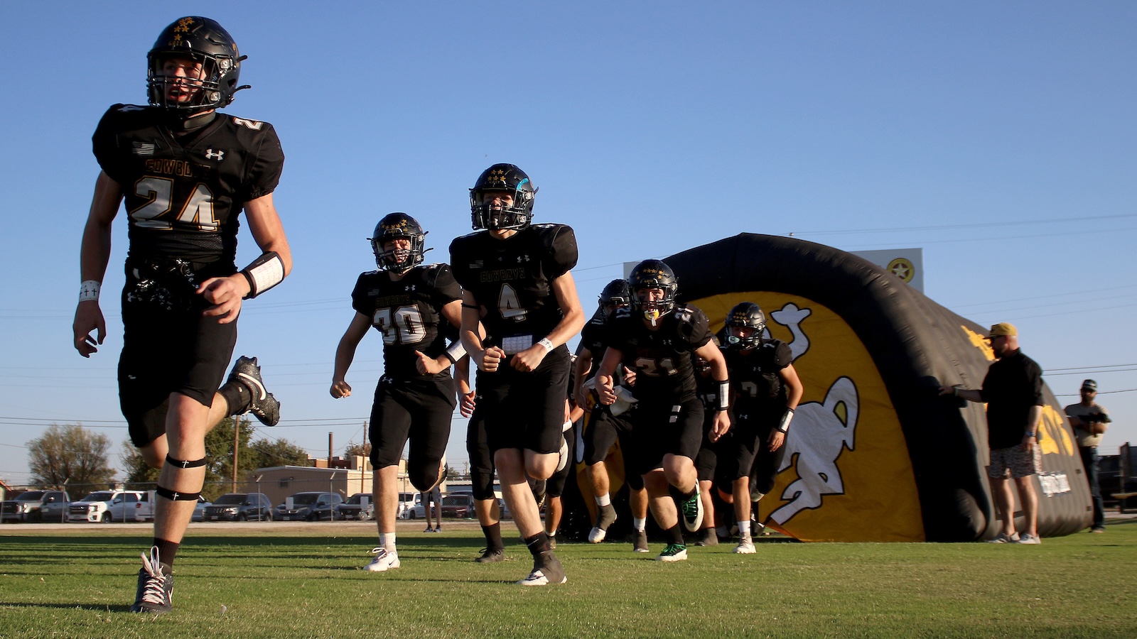 Football players in black uniforms sprint onto the field from a large inflatable tunnel.