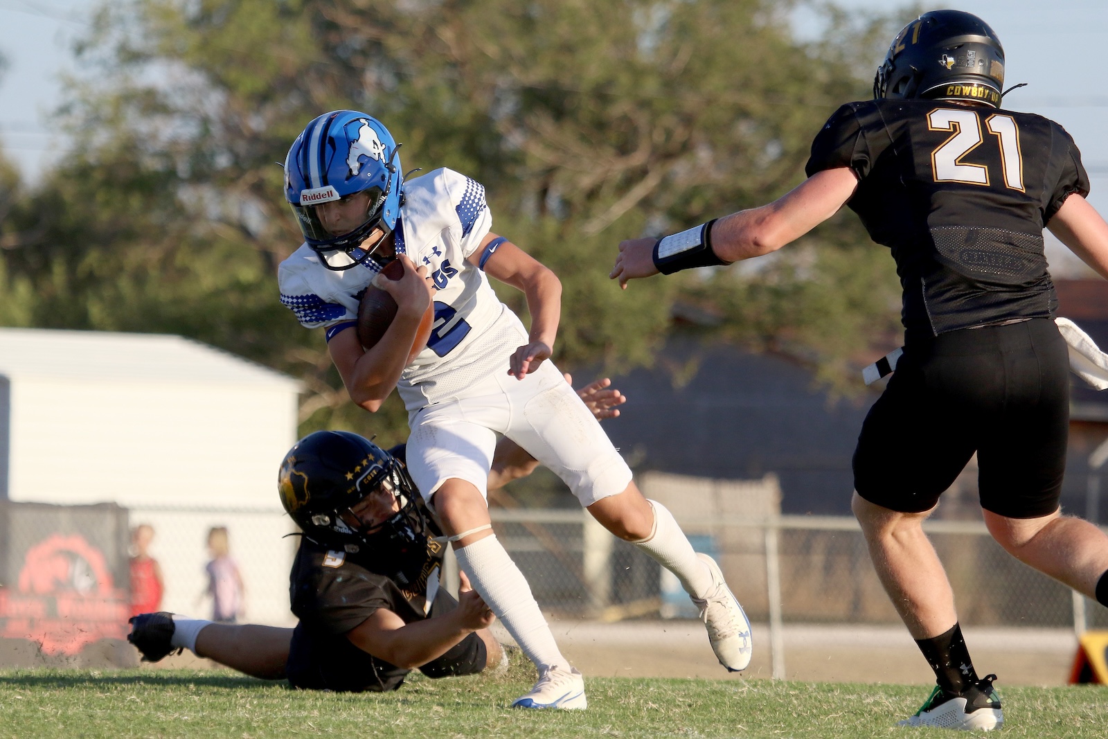 Football player in white uniform running with the ball while a defender in black (number 21) closes in from the right.