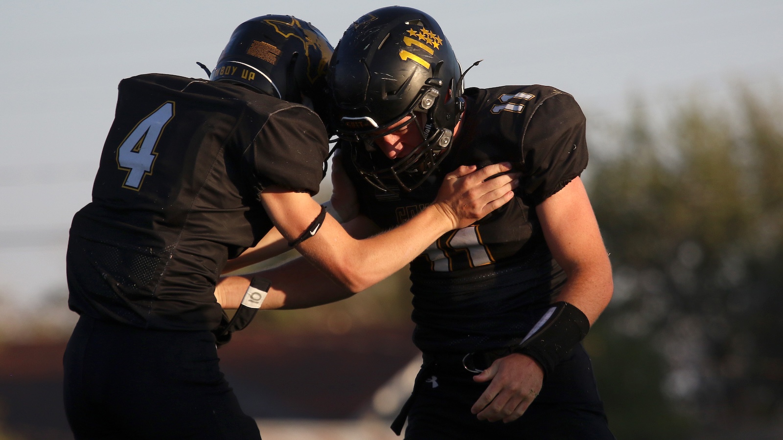 Two football players in black uniforms collide, one wearing number 4, on a sunlit field during a game.