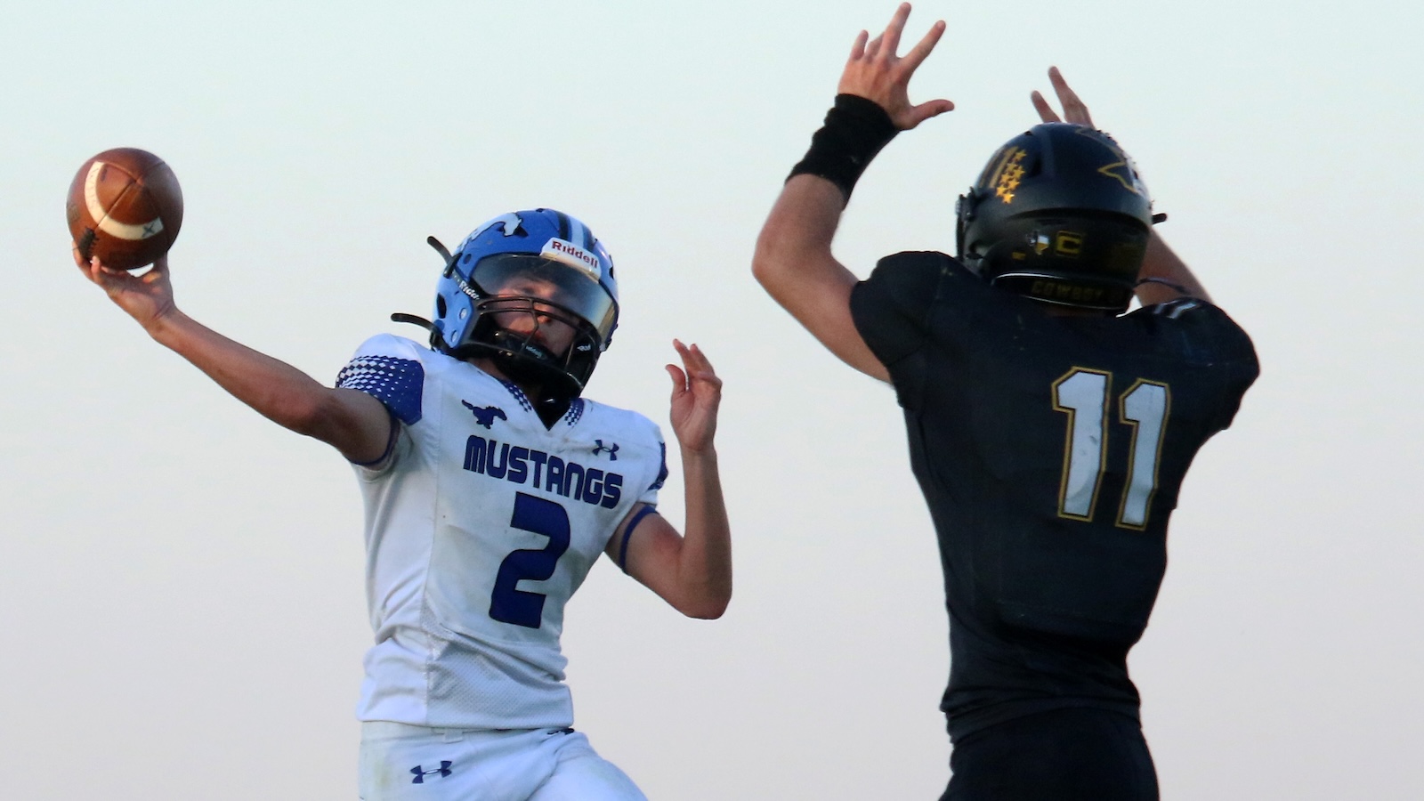 Football players in action: white Mustang jersey quarterback #2 throws a pass as a black‑uniform defender #11 jumps to block him.