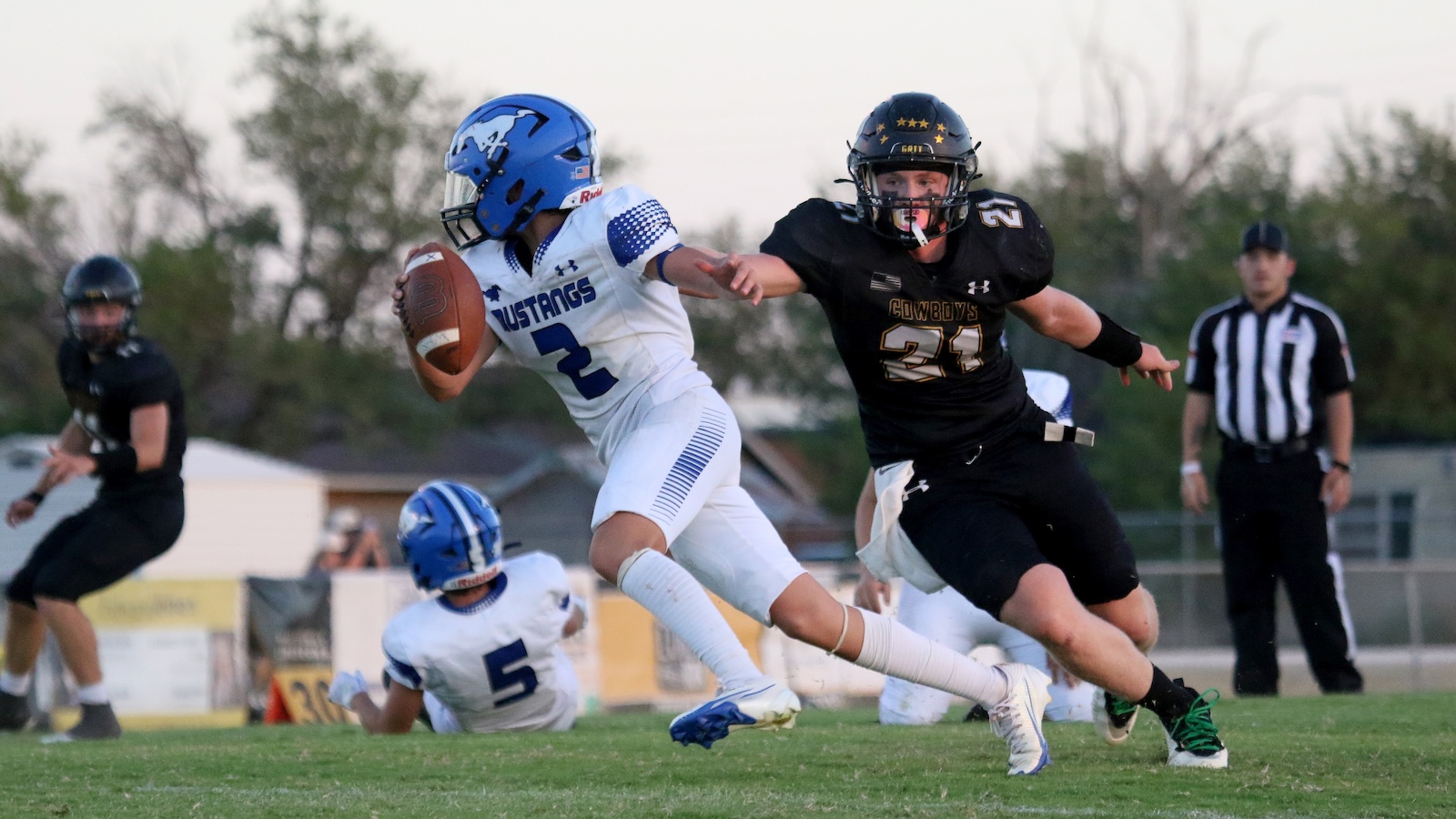 Football action: a white-uniform player with a blue helmet runs with the ball as a black-uniform defender pursues.