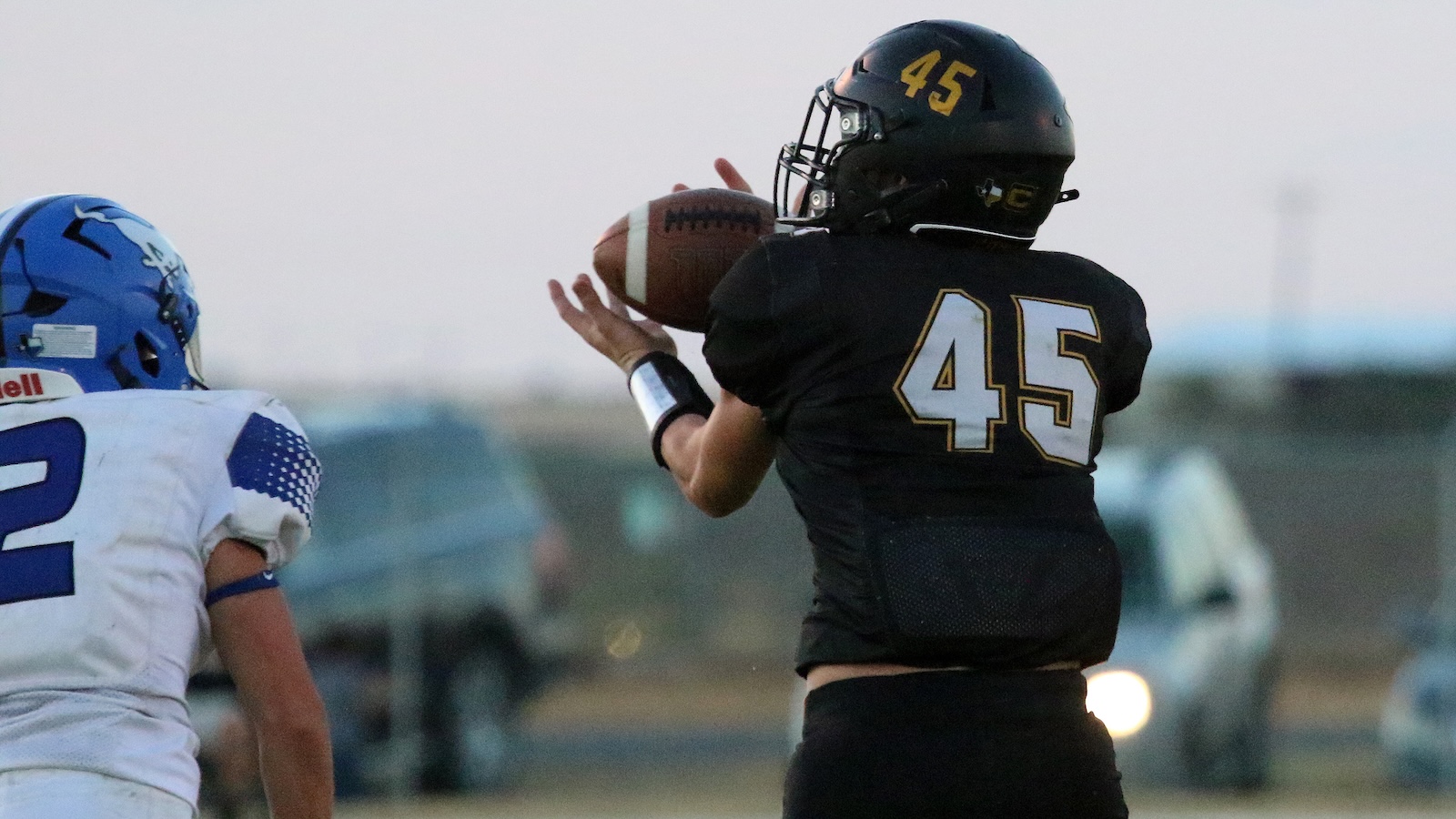 Football player in black jersey #45 attempts to catch a pass, with a blue-helmeted defender close by.