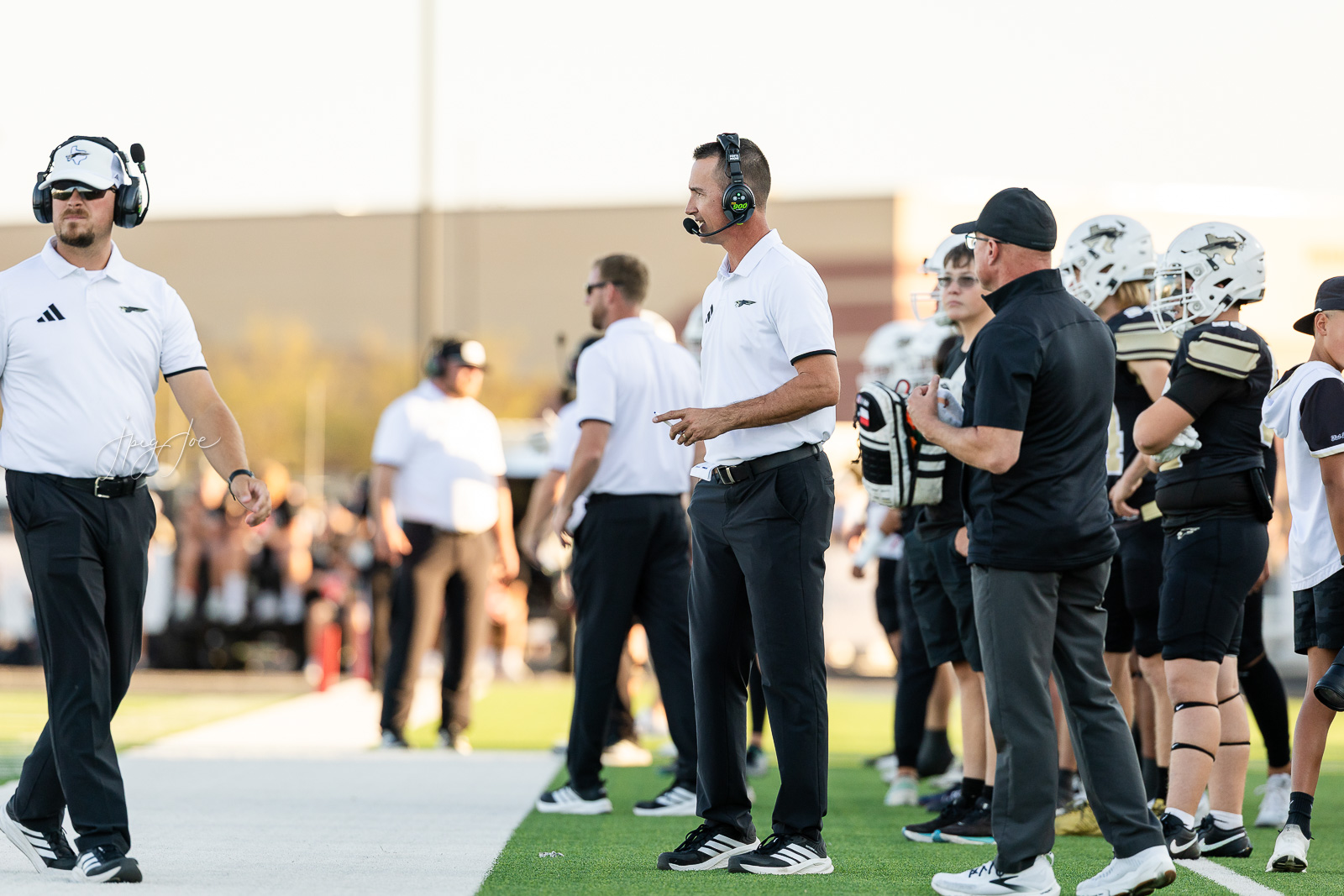 lubbock-christian-vs-bushland-football-jpegJoe-2 | Press Pass Sports Football coach in a white polo with headset on sideline, directing players during a game on a sunny day.