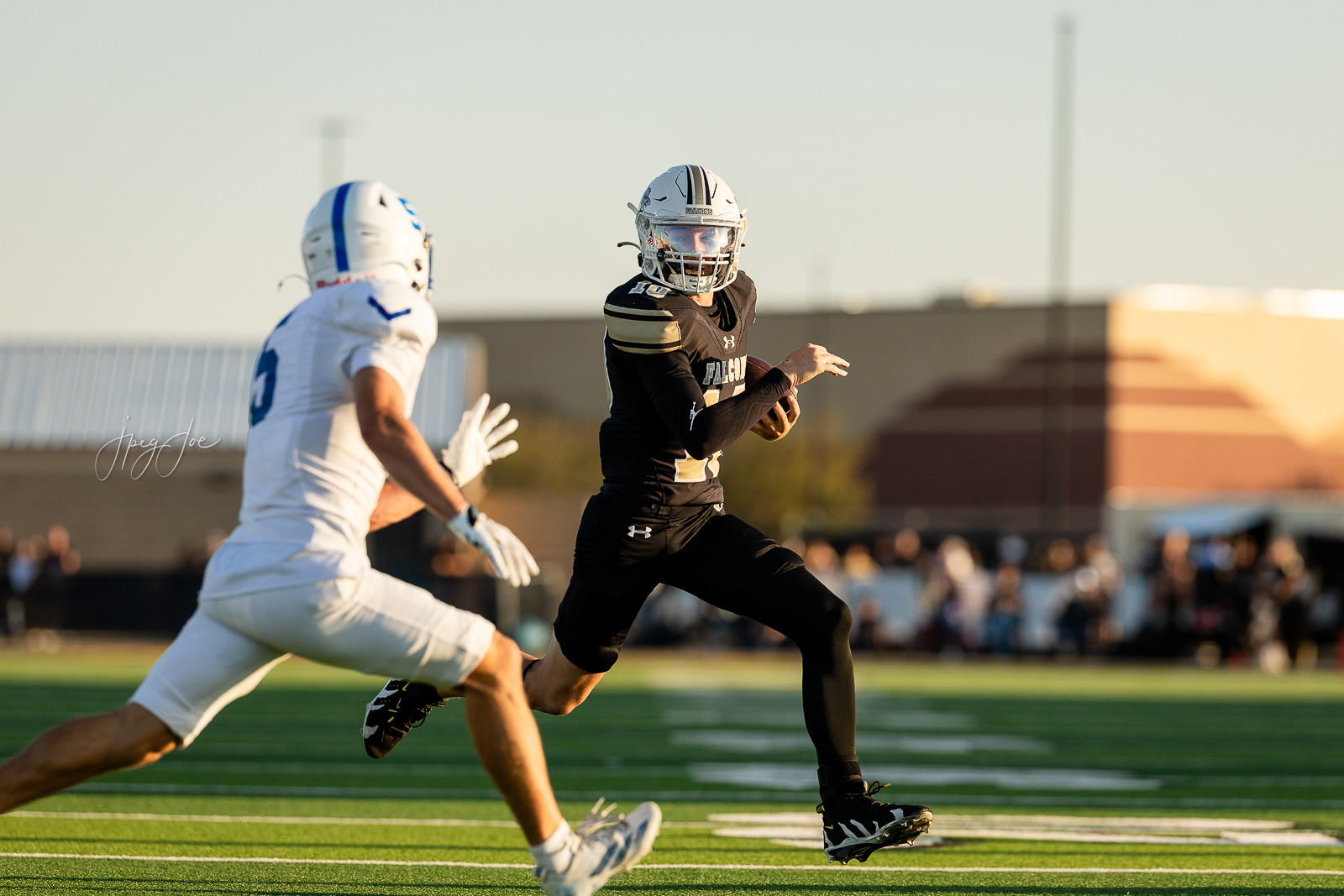 lubbock-christian-vs-bushland-football-jpegJoe-6 | Press Pass Sports Football player in a black Falcons uniform runs with the ball, pursued by a defender in white on a green turf field.