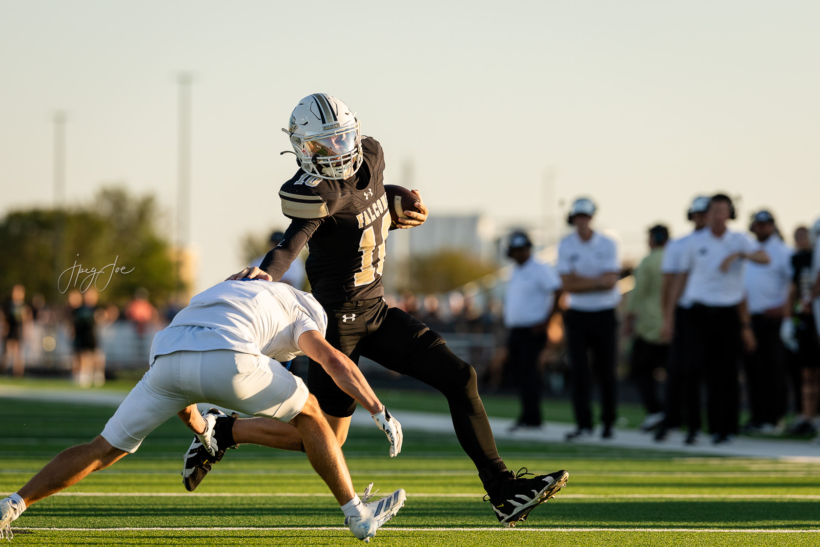 lubbock-christian-vs-bushland-football-jpegJoe-7 | Press Pass Sports Football player in a black Falcons jersey carries the ball while dodging a white-clad defender on a sunny football field.