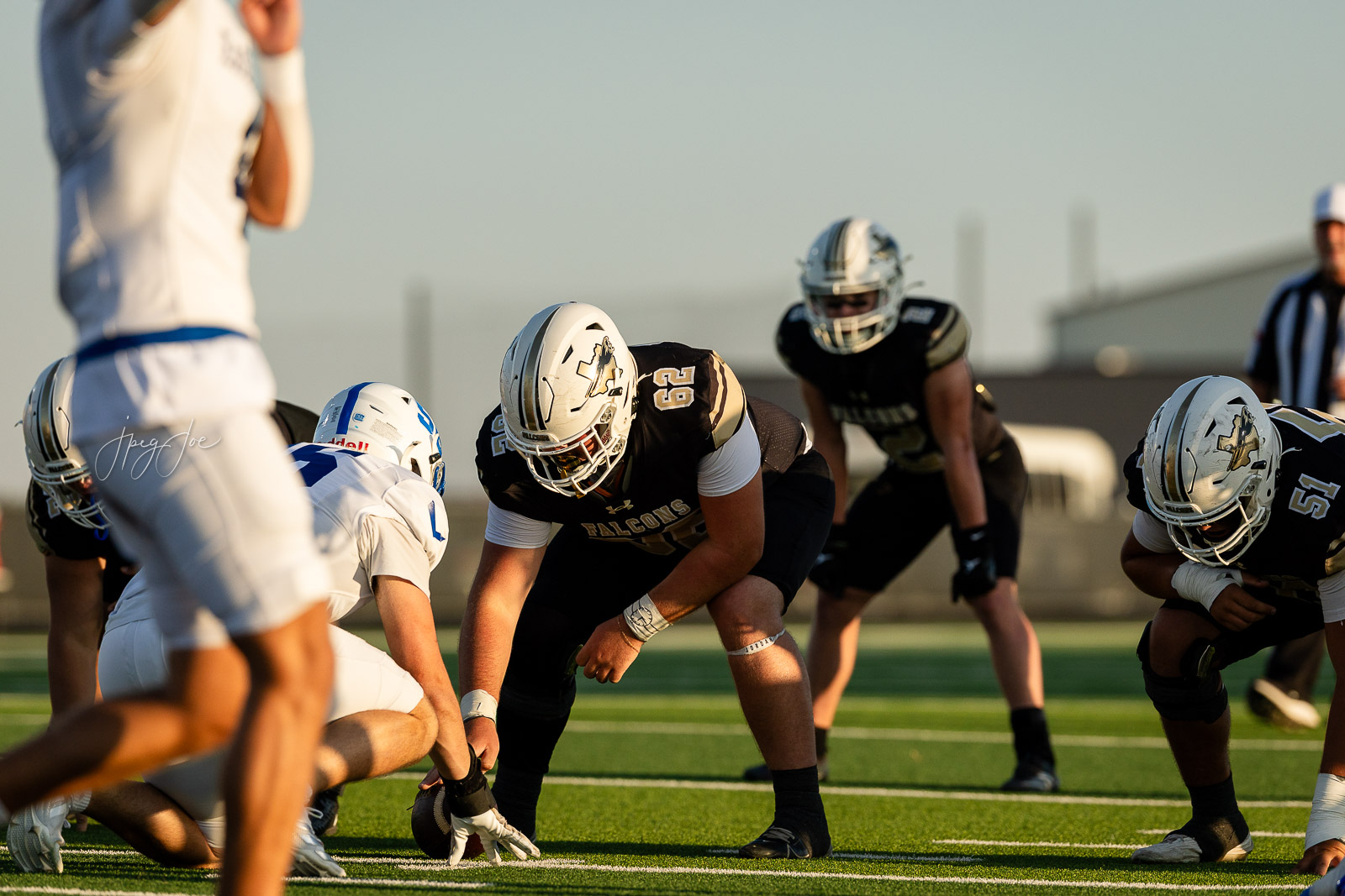lubbock-christian-vs-bushland-football-jpegJoe-8 | Press Pass Sports American football players line up at the line of scrimmage on a sunny field, preparing for the snap.