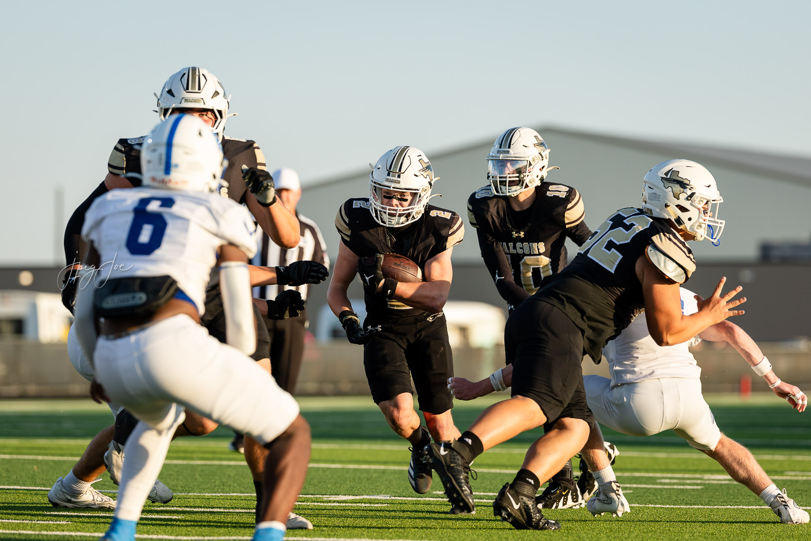 lubbock-christian-vs-bushland-football-jpegJoe-9 | Press Pass Sports Running back in black, gold-and-white uniform holds the ball and runs through a crowd of defenders on a sunny football field.