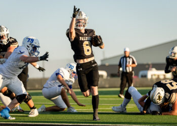 lubbock-christian-vs-bushland-football-jpegJoe-11 | Press Pass Sports Falcons player in black #6 leaps with ball as he runs toward the end zone during a daytime football game; defenders in white nearby and a referee in the background.
