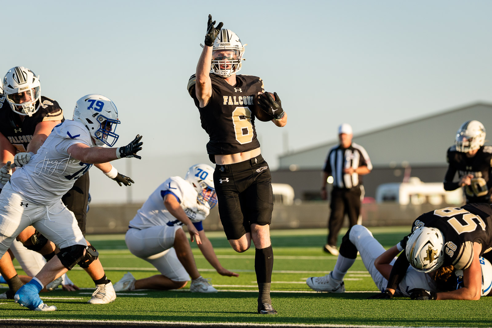lubbock-christian-vs-bushland-football-jpegJoe-11 | Press Pass Sports Falcons player in black #6 leaps with ball as he runs toward the end zone during a daytime football game; defenders in white nearby and a referee in the background.