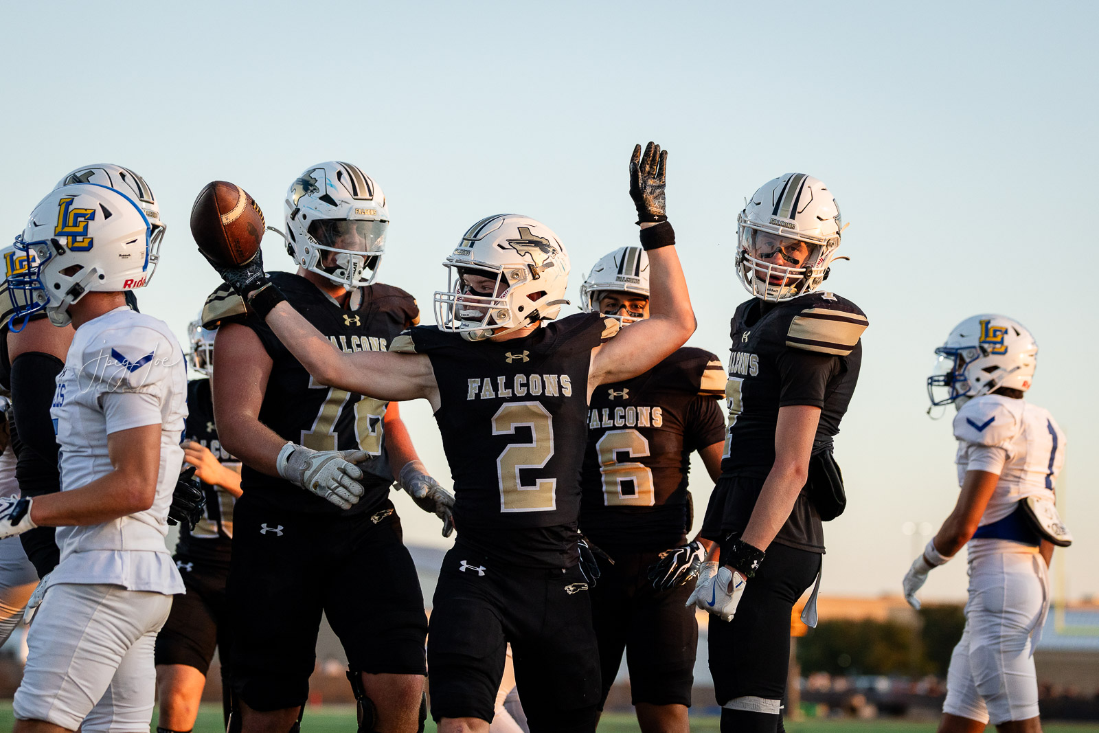 lubbock-christian-vs-bushland-football-jpegJoe-23 | Press Pass Sports Falcons football players in black uniforms celebrate on the field with arms raised during a game. White-helmeted teammates surround a central player wearing number 2.
