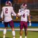 Simmons ASU | Press Pass Sports Two football teammates in white maroon uniforms give a high-five on a green field with bleachers in the background, celebrating.