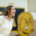 IMG_7524 | Press Pass Sports Woman in a white shirt laughing or shouting in a gym setting, with a large yellow mascot logo blurred in the background.