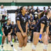Volleyball players in black uniforms celebrate on the court, foreground player with number 3 shouting.