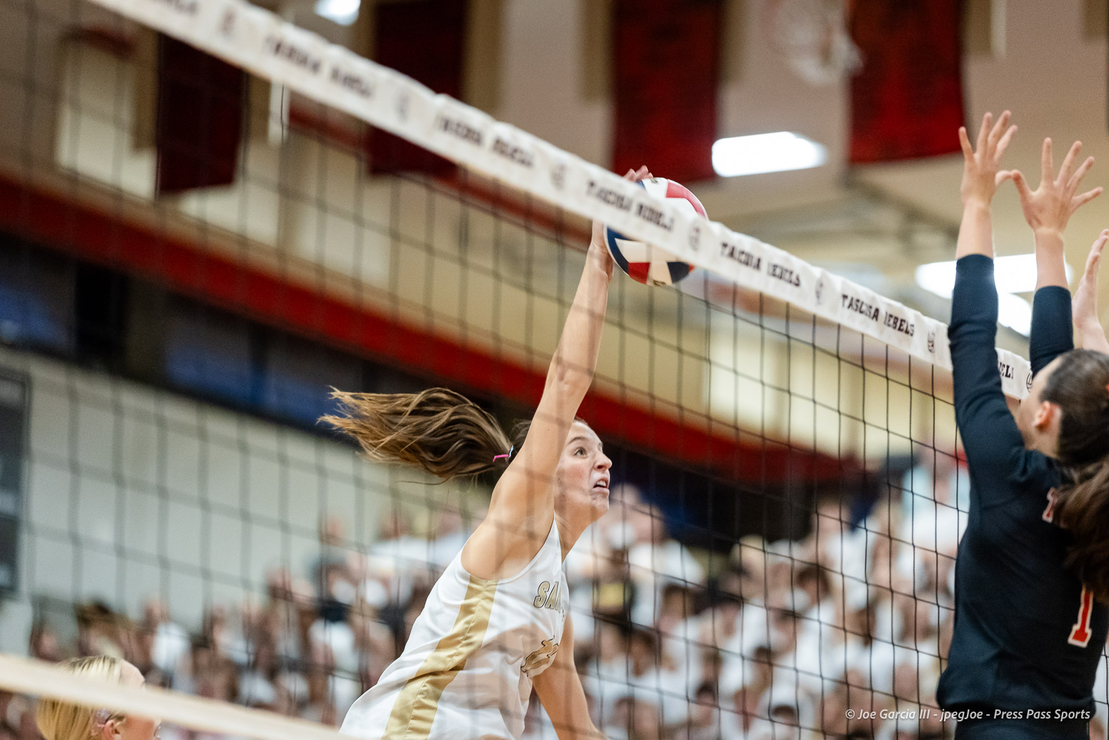 amarillo-high-vs-tascosa-volleyball-jpegJoe-pps-8 | Press Pass Sports Female volleyball player in white and gold spikes the ball over the net as a defender jumps to block at the net
