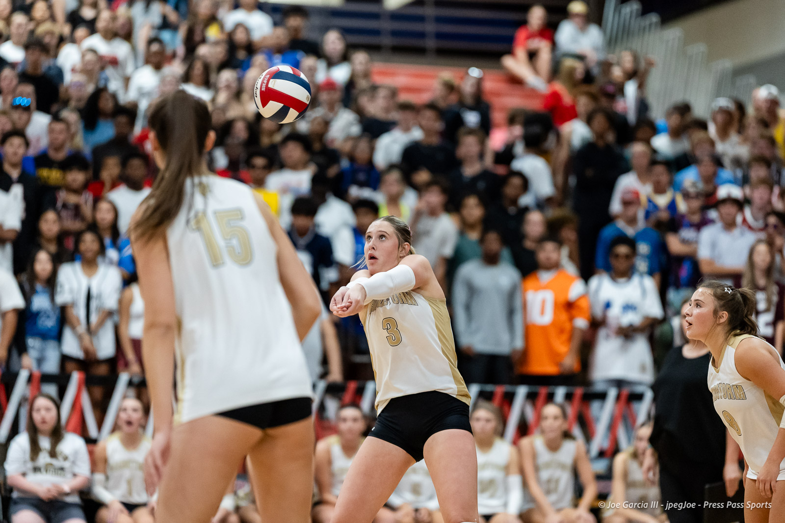 amarillo-high-vs-tascosa-volleyball-jpegJoe-pps-15 | Press Pass Sports Action shot of a women's indoor volleyball match: player wearing number 3 in beige dives with arms extended to receive the ball as a ball sails overhead, crowded bleachers in the background.
