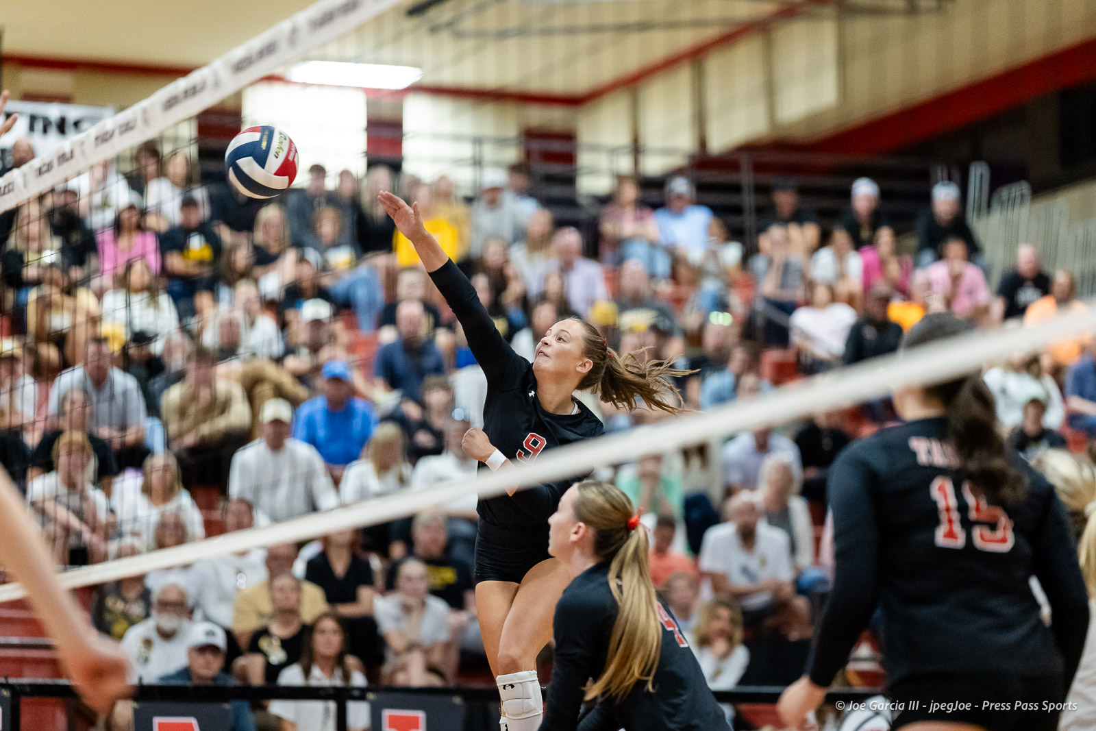 amarillo-high-vs-tascosa-volleyball-jpegJoe-pps-16 | Press Pass Sports Female volleyball player jumps to spike the ball over the net during a crowded indoor match.