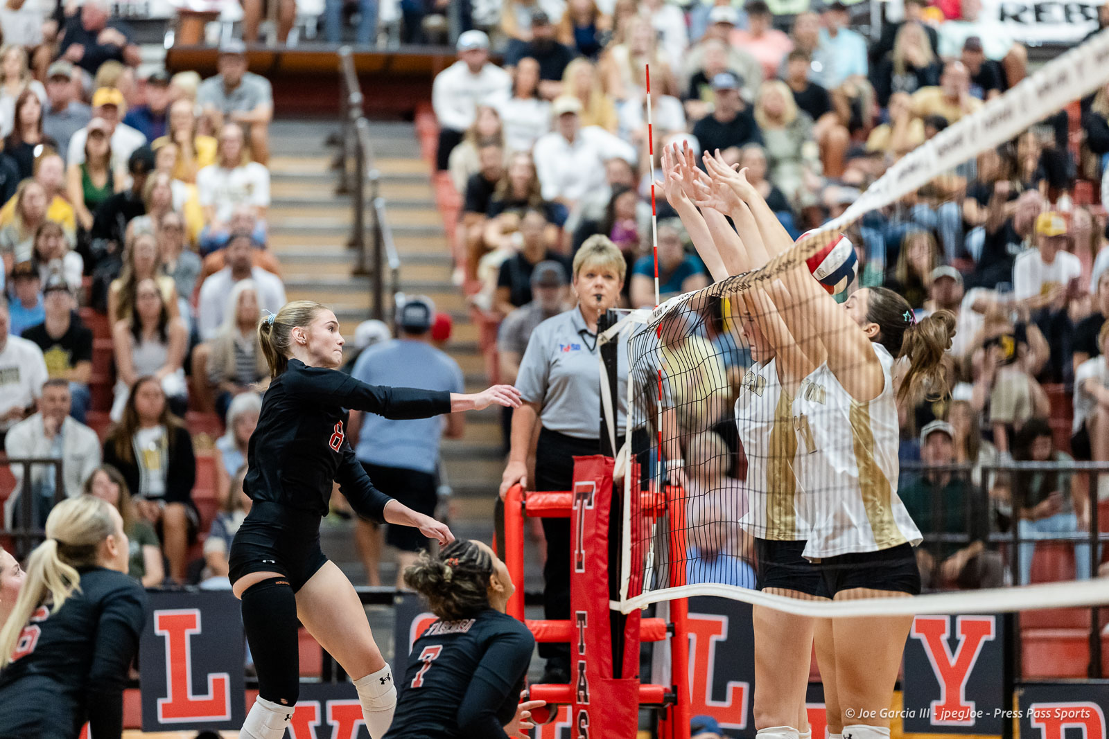 amarillo-high-vs-tascosa-volleyball-jpegJoe-pps-17 | Press Pass Sports Female volleyball player in black uniform spikes the ball over the net as teammates defend, with a crowded gym audience in the background.