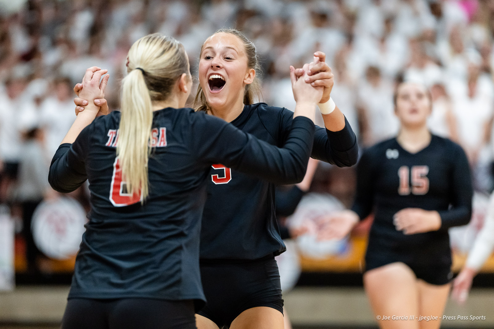 amarillo-high-vs-tascosa-volleyball-jpegJoe-pps-19 | Press Pass Sports Two female volleyball players in dark uniforms celebrate with a high-five on the court as a cheering crowd watches.