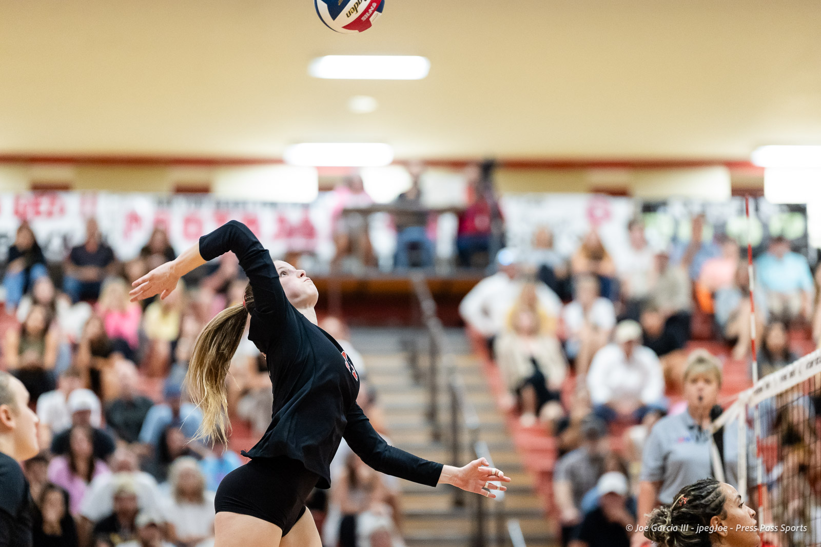 amarillo-high-vs-tascosa-volleyball-jpegJoe-pps-21 | Press Pass Sports Female volleyball player in black rallies a ball with an overhead swing in a gym, crowd blurred in the stands behind her