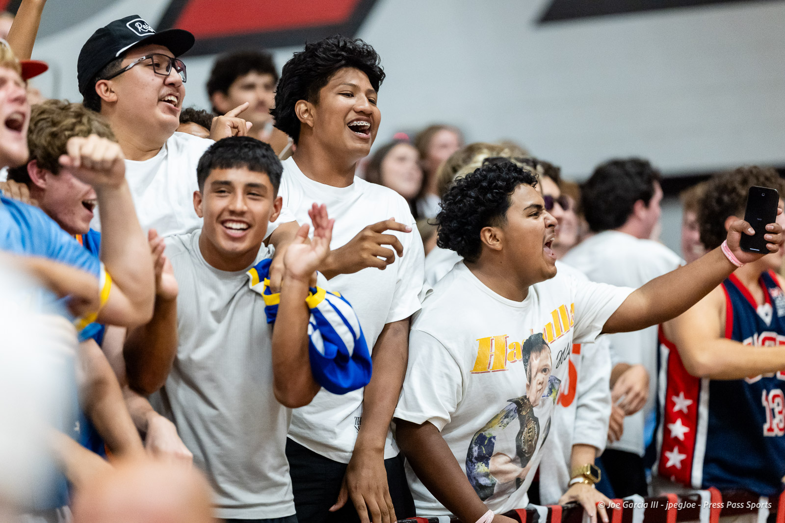amarillo-high-vs-tascosa-volleyball-jpegJoe-pps-25 | Press Pass Sports Group of enthusiastic cheerleaders and fans at a sports event, raising arms and smiling. A person on the right holds up a phone to record the moment.