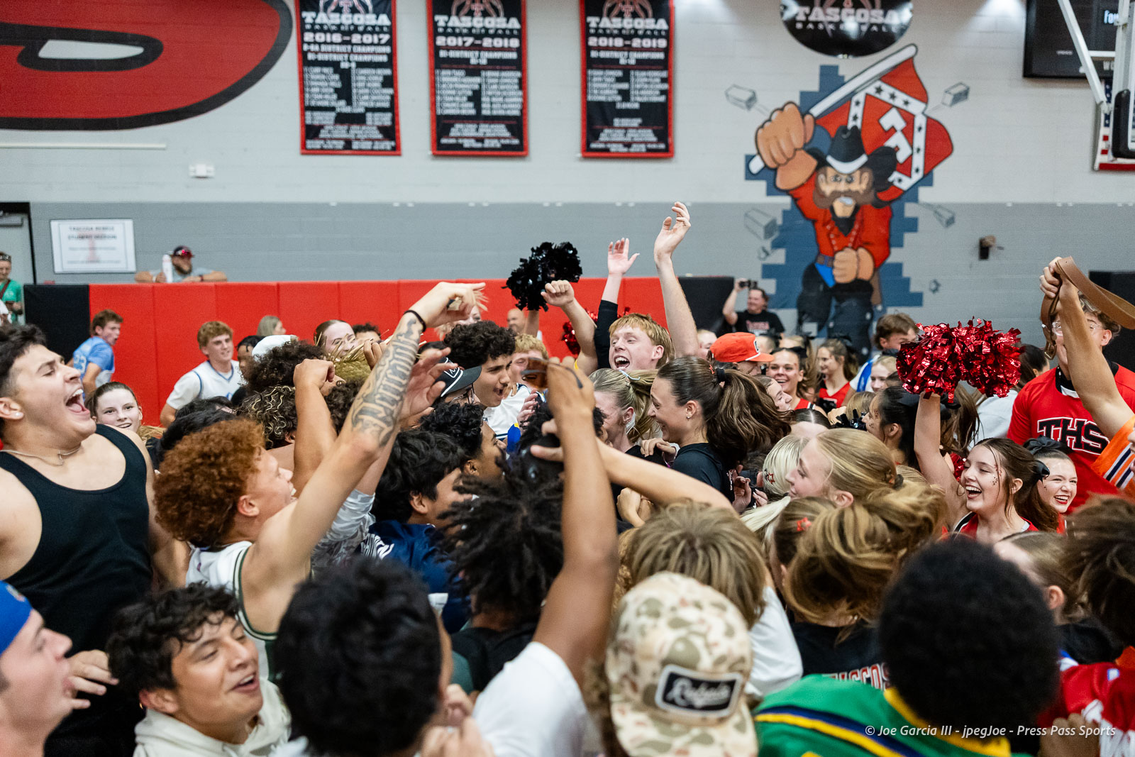 amarillo-high-vs-tascosa-volleyball-jpegJoe-pps-26 | Press Pass Sports Large group of students in a school gym cheering with raised arms and red pom-poms, energetic crowd scene amid banners and a pirate mural on the wall