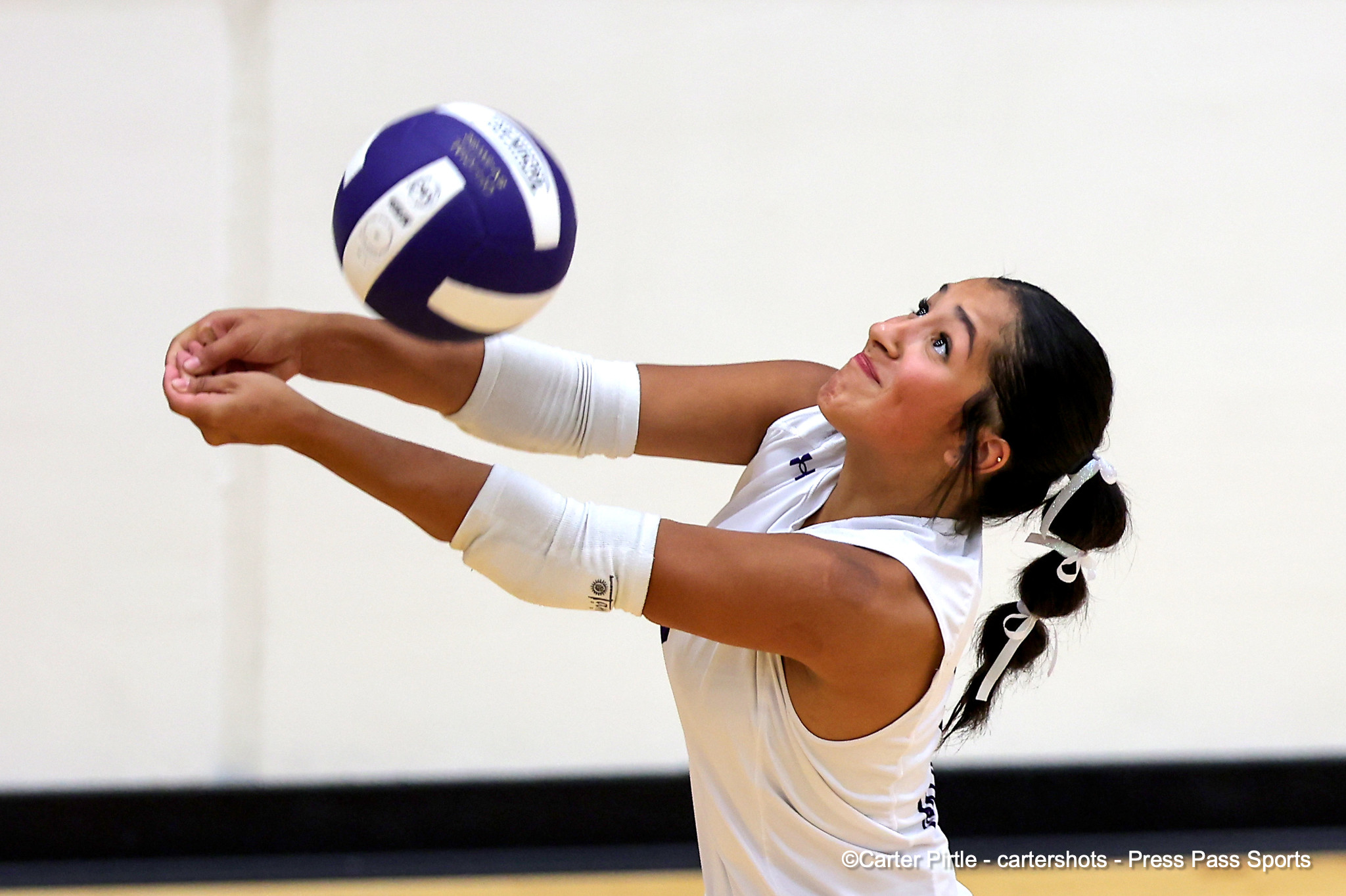 Female volleyball player in white uniform diving to bump the ball, arms extended, indoors.
