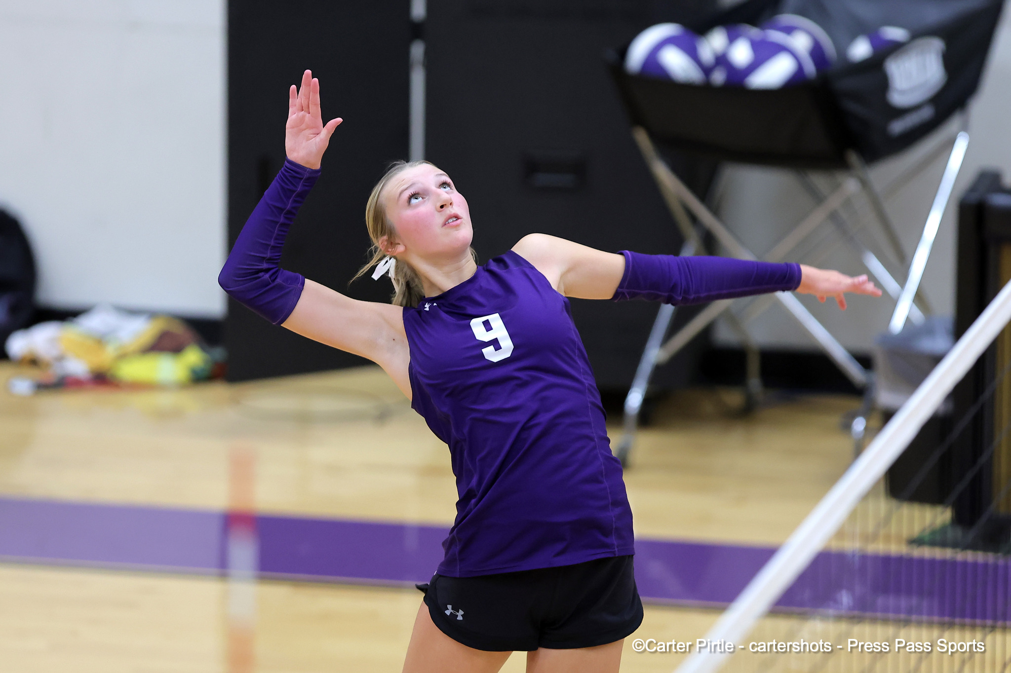 Female volleyball player in a purple uniform (number 9) raises both arms in a dynamic pose on an indoor court.