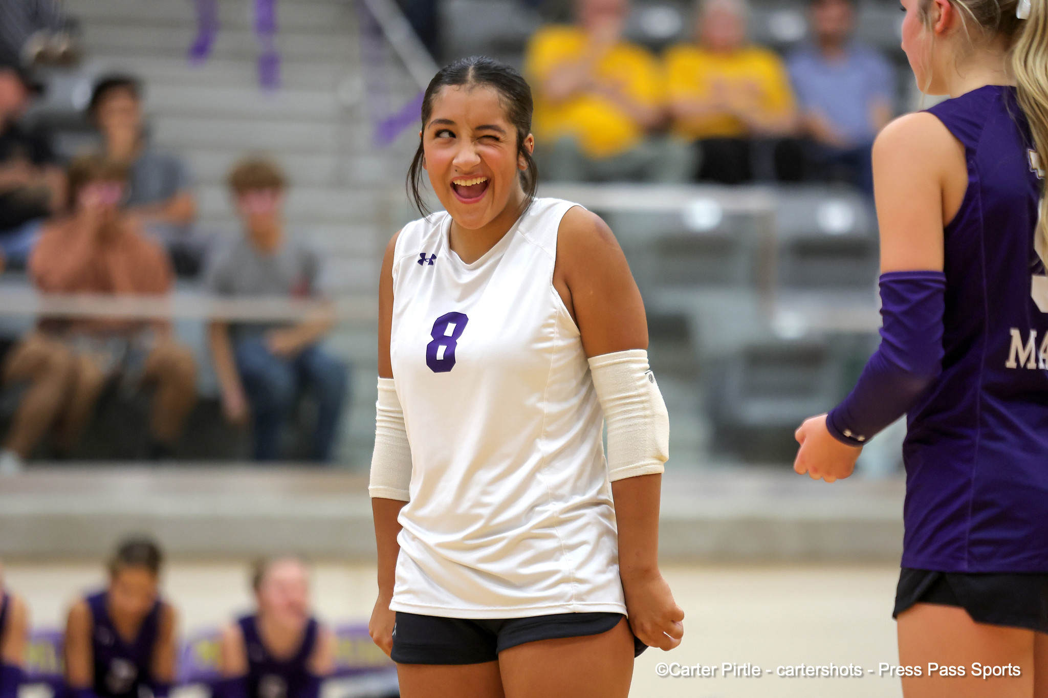 Volleyball player in white #8 smiling and winking during a match with teammates in the background.
