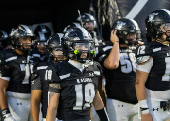 CHS-RHS-FB-2 1 | Press Pass Sports Raiders football players in black and white uniforms gather in a tunnel, foreground player wearing number 19 and neon green mouthguard.