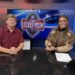 Two TV hosts sit at a desk in a studio, with a large screen showing the 'The Locker Room' logo behind them.