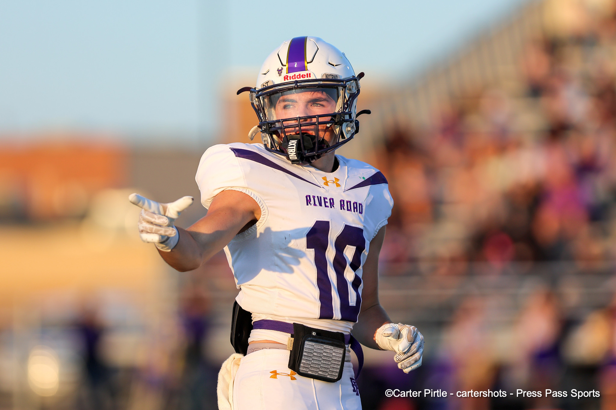 Football player in white and purple uniform raises an arm in celebration on the field, helmet on.