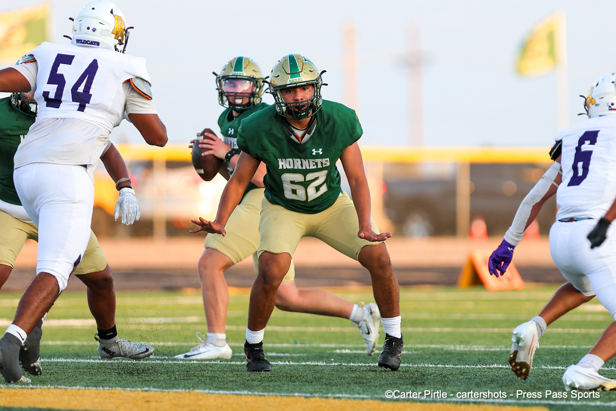 A football player in a green Hornets jersey (#62) lunges forward as teammates and opponents close in on the field.