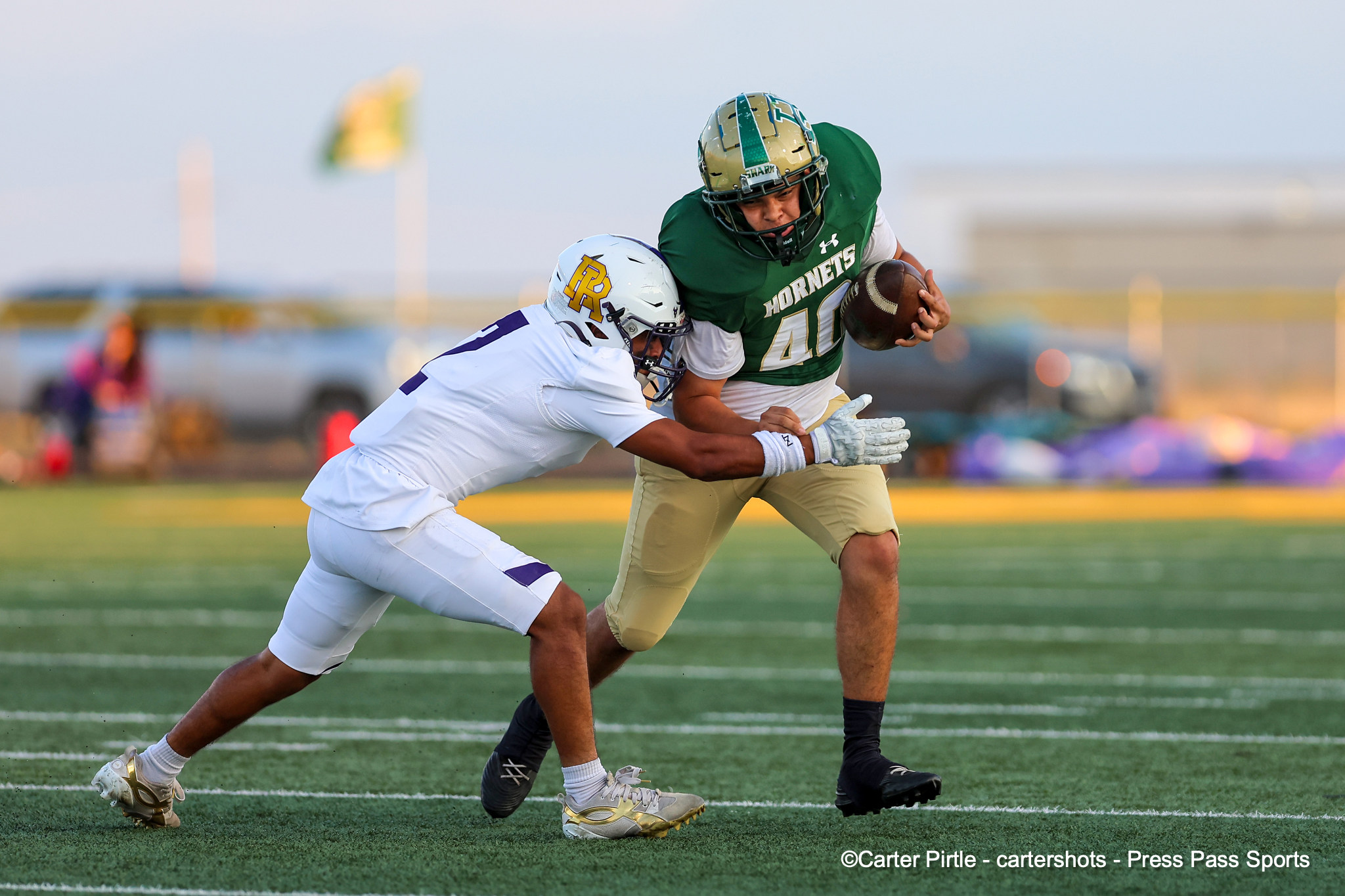 Green Hornets running back carries the ball while a white-team defender dives in for a tackle on a grassy field.