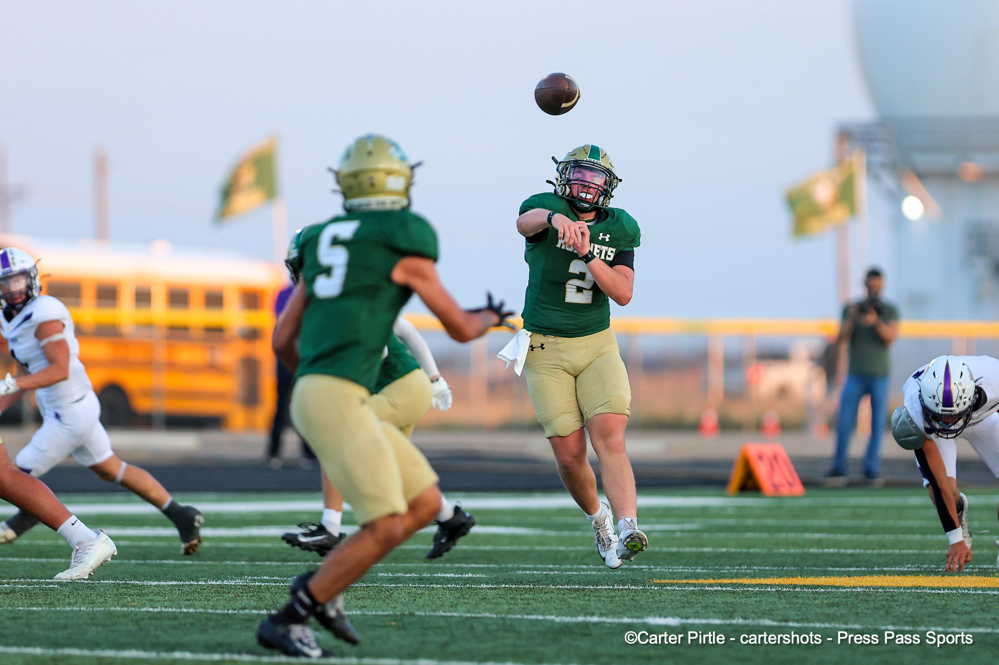A football quarterback in a green uniform throws a pass as teammates and defenders reach for the ball on a football field.
