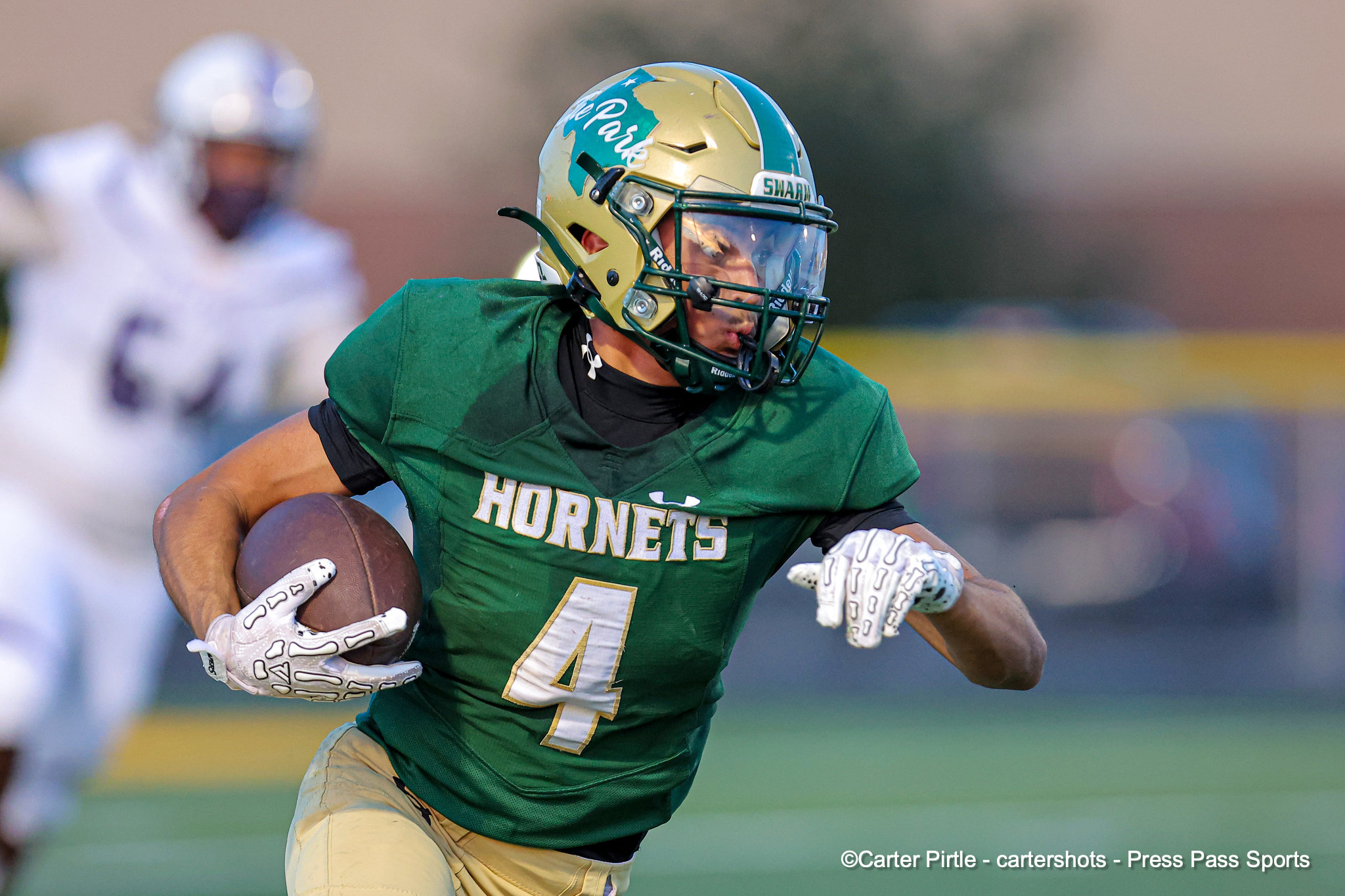Football player in a green Hornets uniform runs with the ball during a game, wearing a gold helmet with a teal stripe.