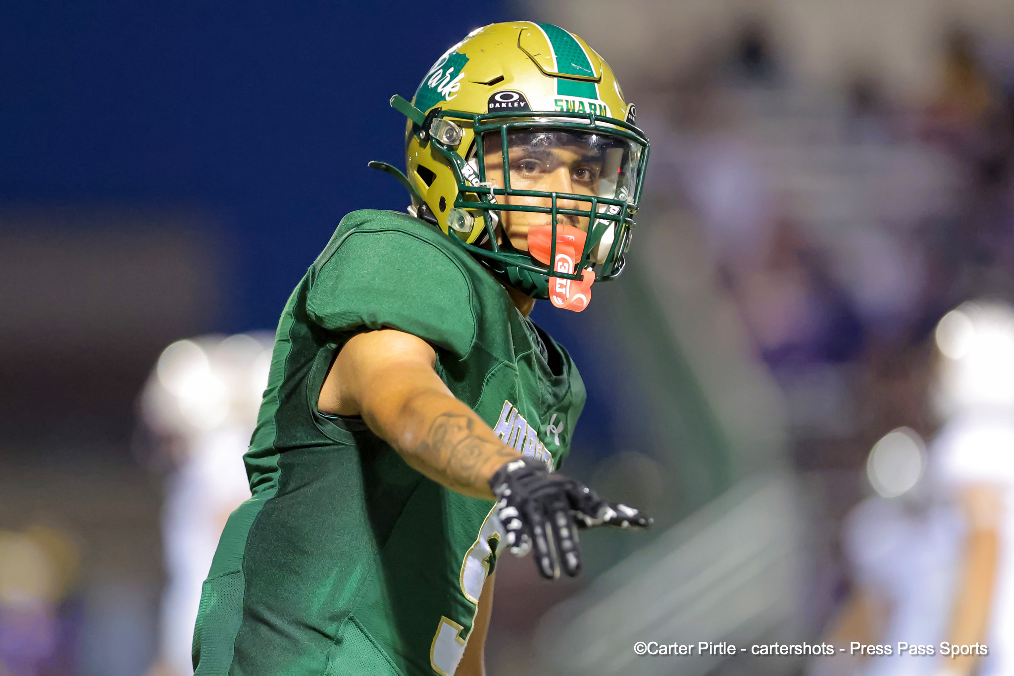 Football player in a green jersey and yellow helmet raising a clenched fist and pointing forward mid-game