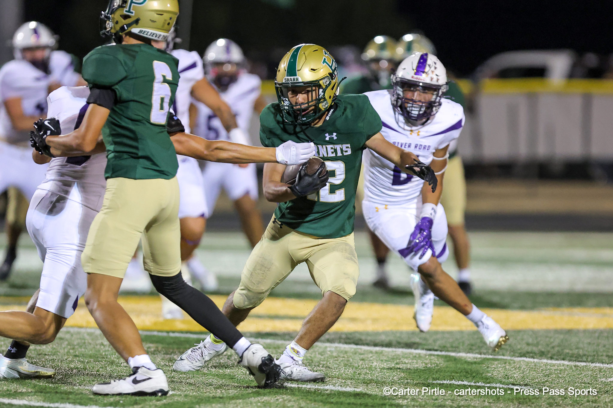Hornets player in green carries the ball while teammates block during a night football game.