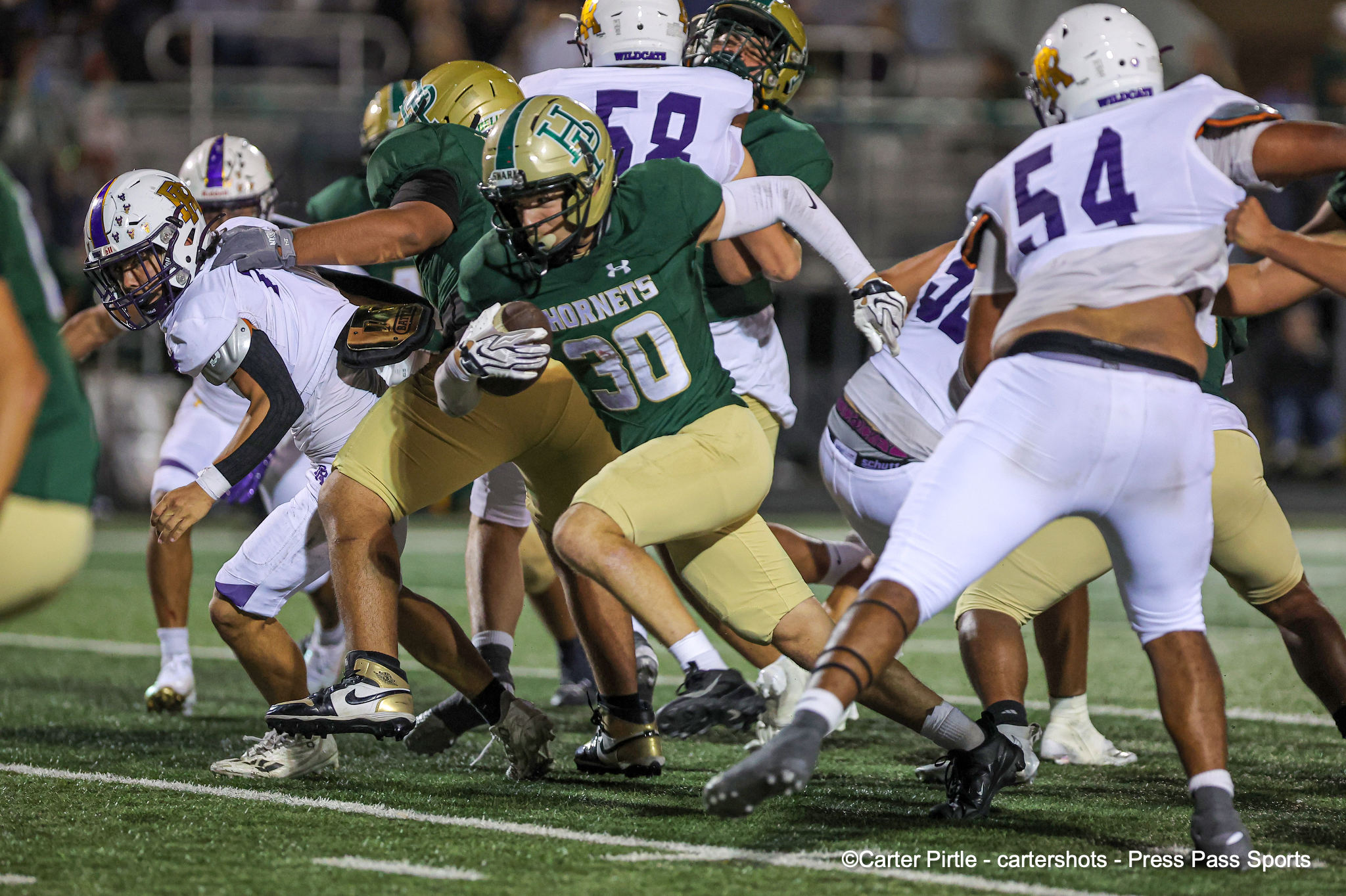 Green Hornets ball carrier dodges through a pile of white-uniform players during an intense football play.