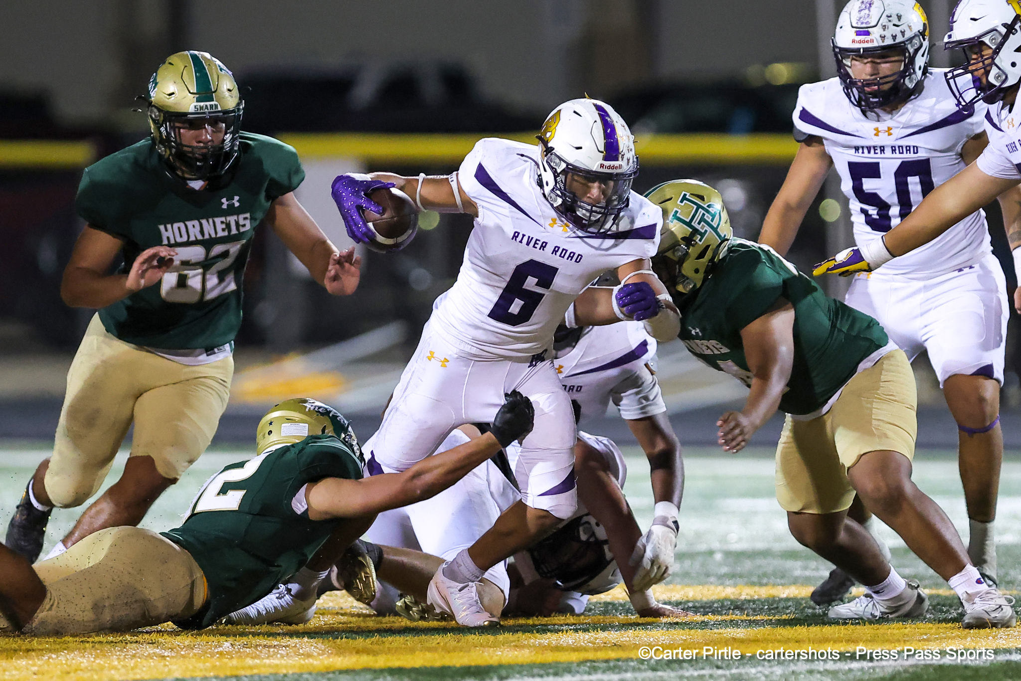 River Road running back (white jersey) carries the ball as defenders close in during a nighttime high school football game against the Hornets.