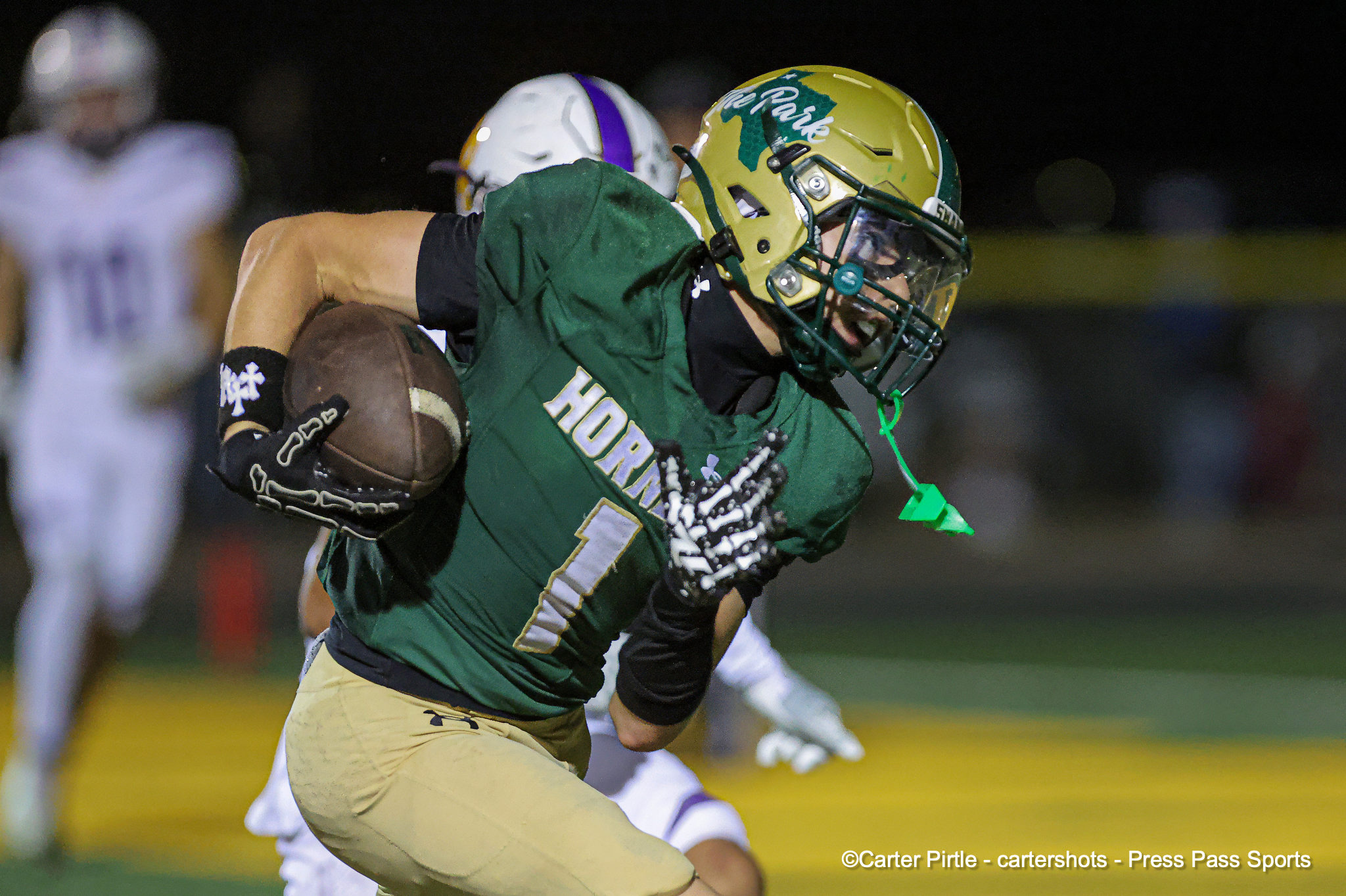Football player in green uniform runs with the ball during a nighttime game, helmet worn, action shot on the field.