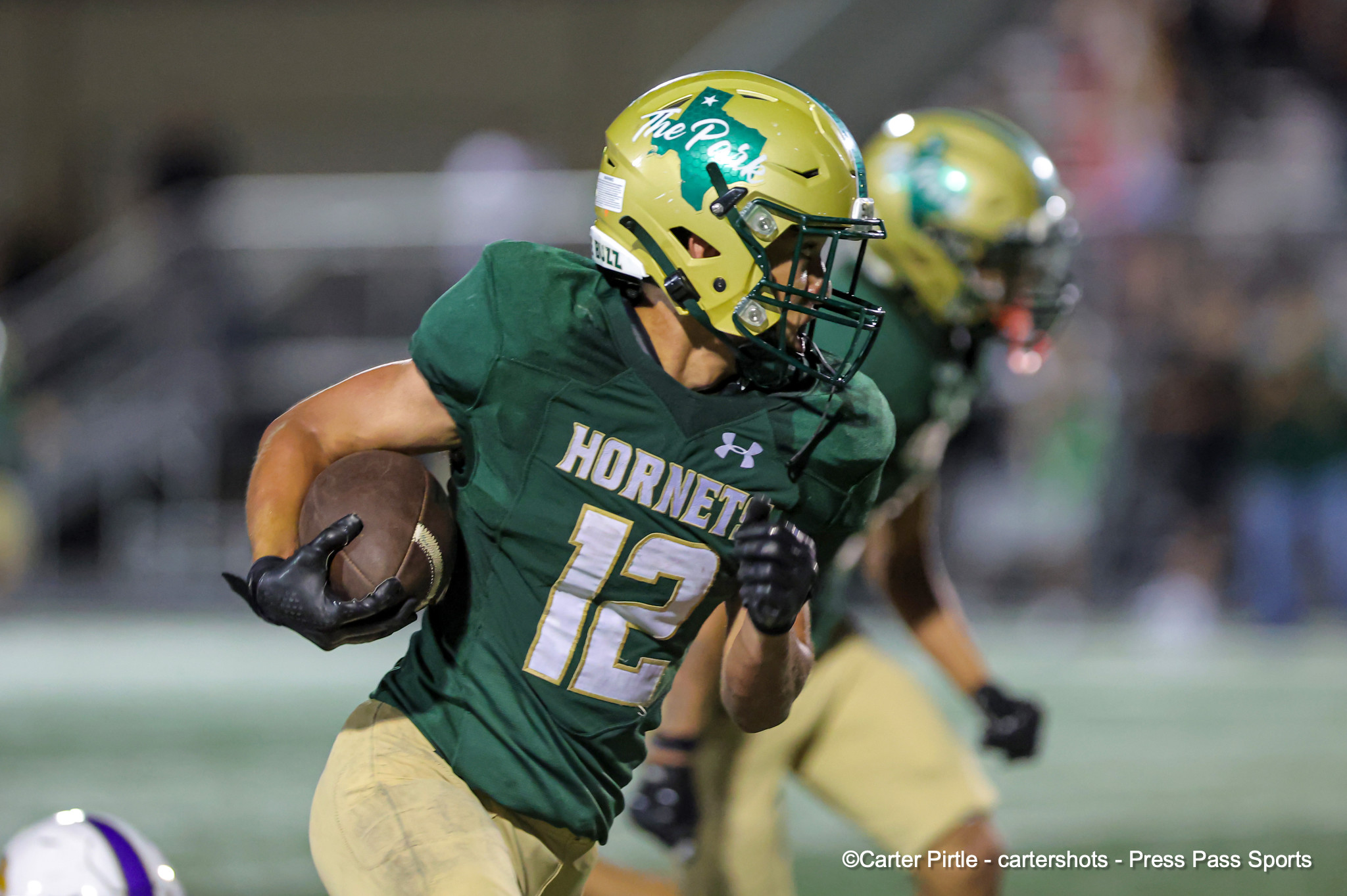 Football player in a green Hornets uniform runs with the ball during a game, wearing a yellow helmet with a green face guard and #13.