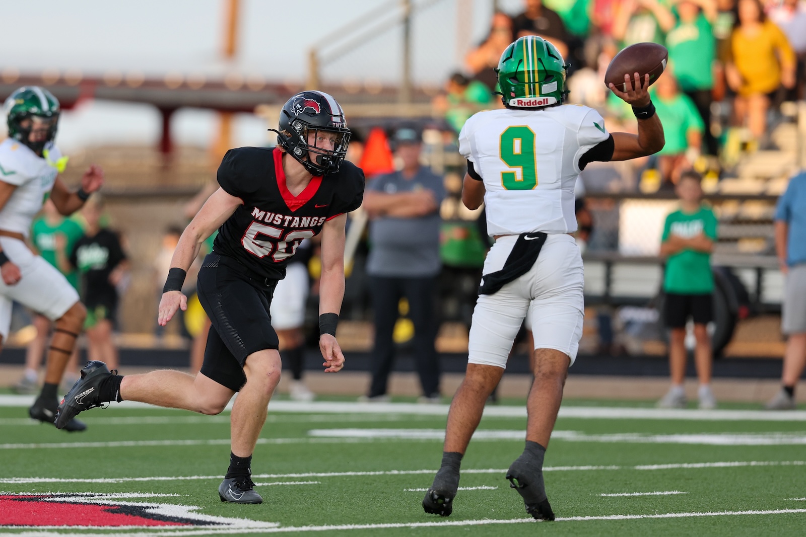 Seabolt Chase-16667 | Press Pass Sports Football game action: a player in a black Mustang jersey (#66) runs toward a white-jersey opponent as he throws a pass on a green turf field.